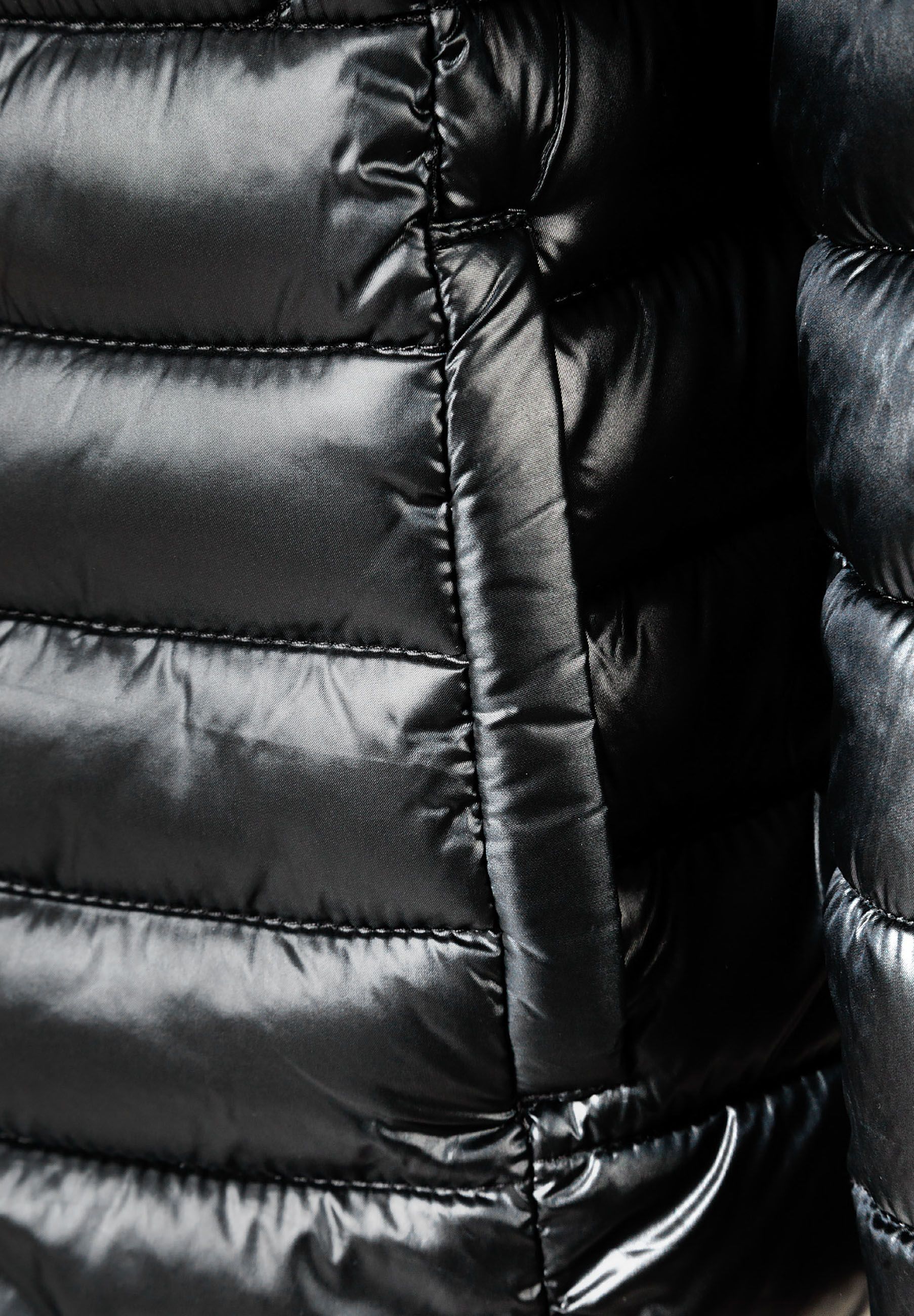 Detail of a black quilted girls jacket with zip fastening and side pocket.