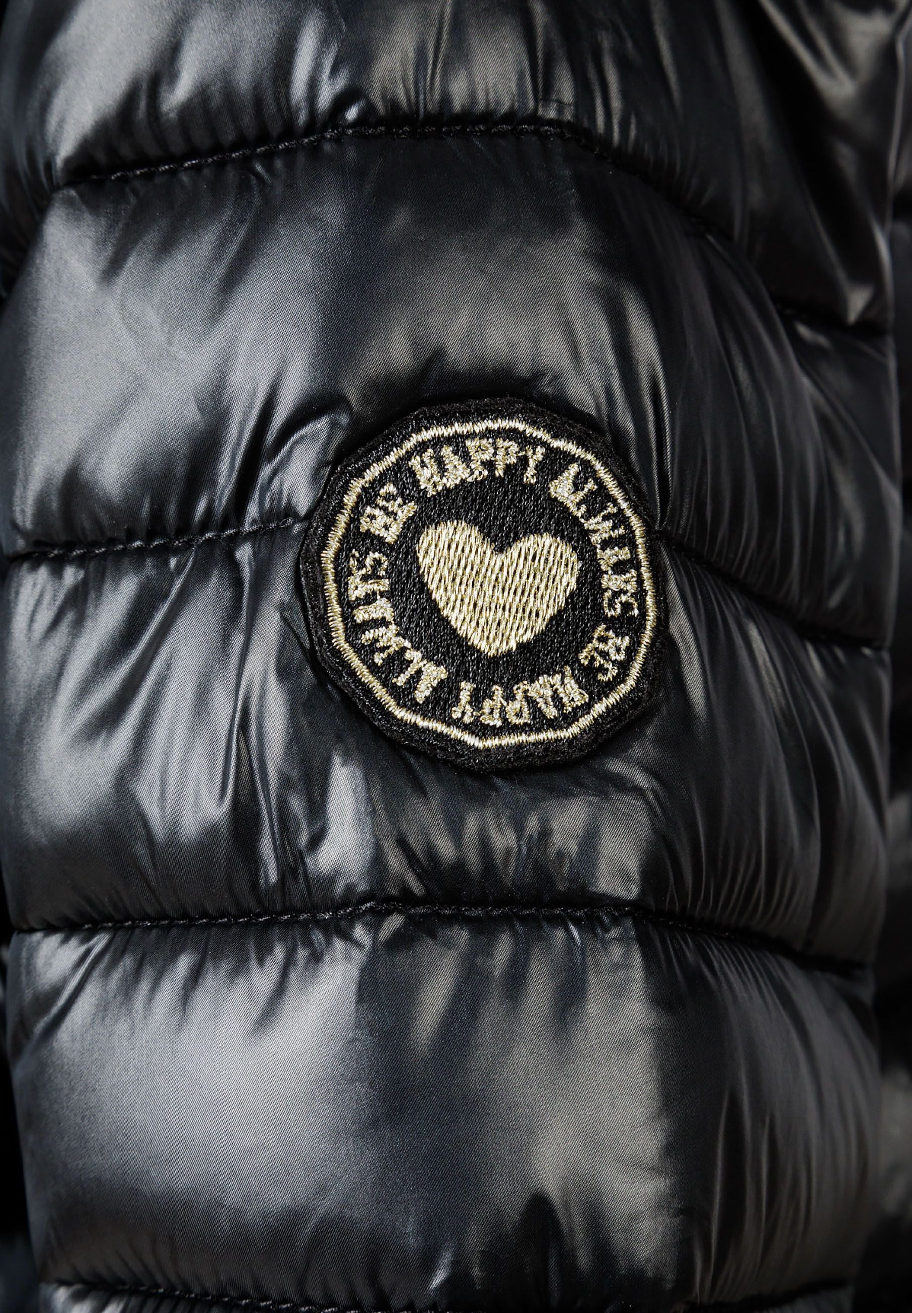 Detail of a black quilted jacket with a heart-shaped badge.
