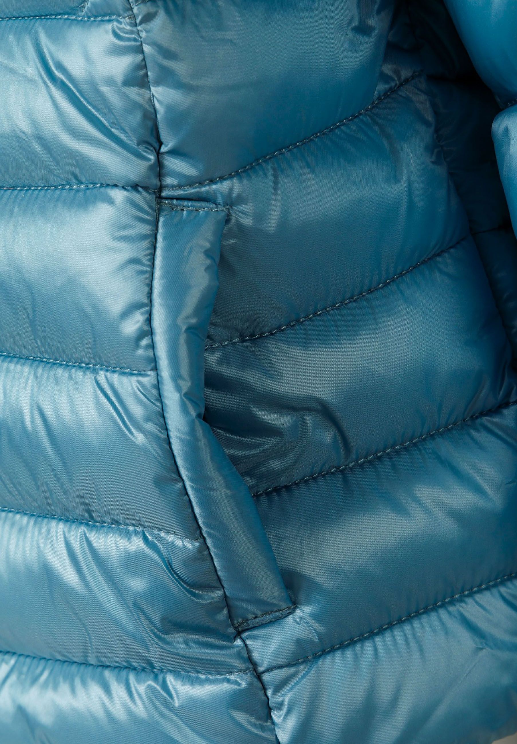 Detail of a quilted turquoise girls jacket with a fixed hood and zip fastening.