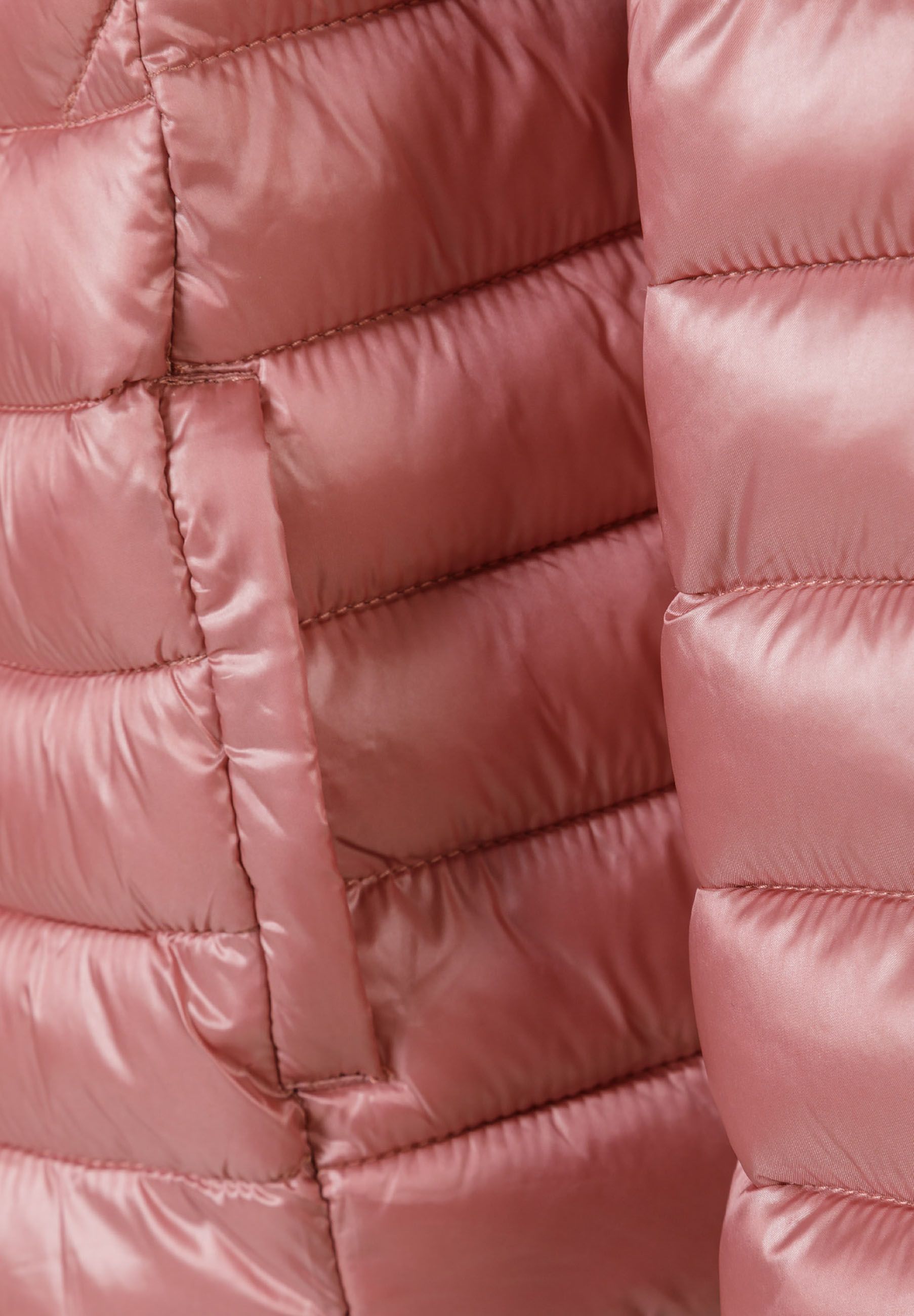 Detail of a quilted girls' jacket in soft pink with a heart-shaped badge.