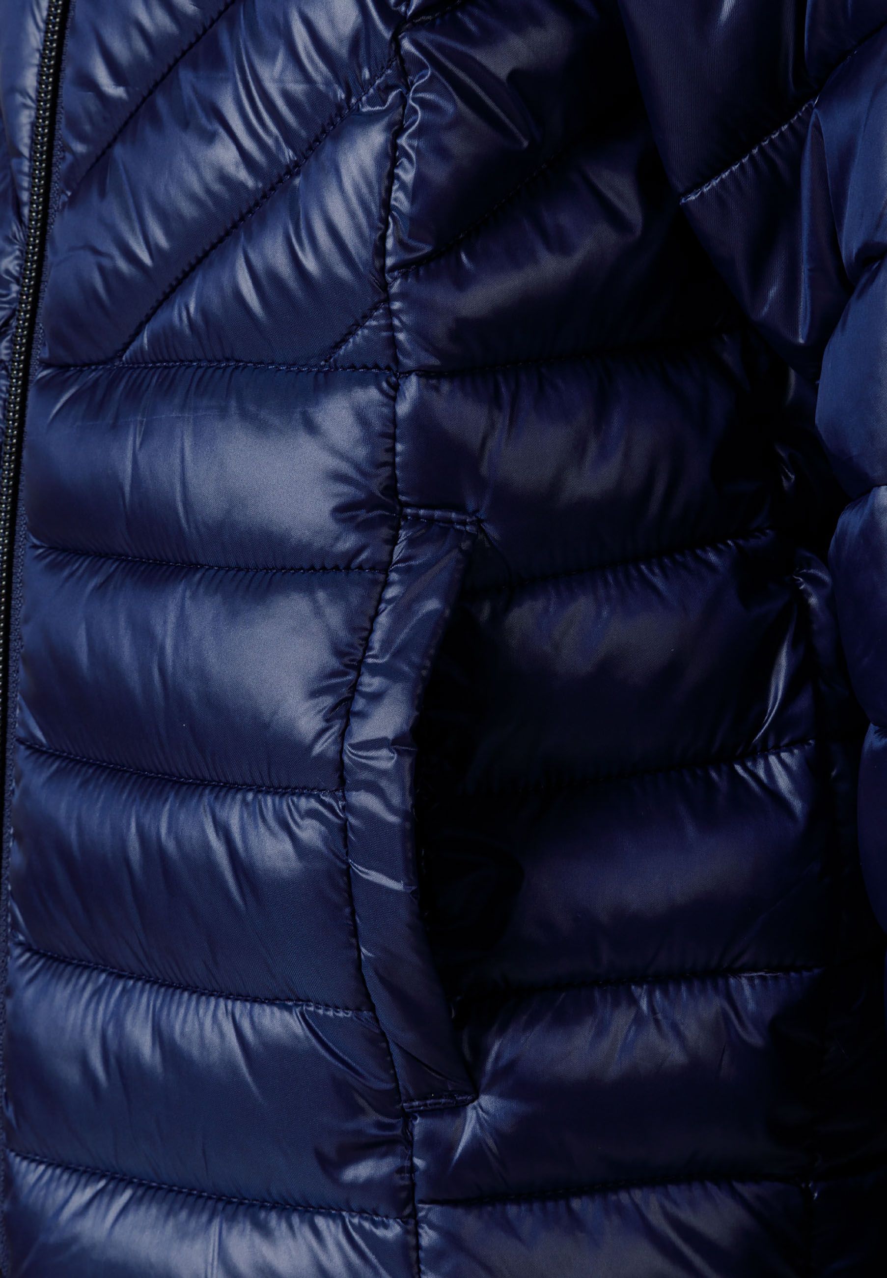 Detail of a navy quilted girls jacket showing padding and side pocket.