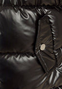 Detail of a shiny black winter coat showing a flap pocket with a snap closure.
