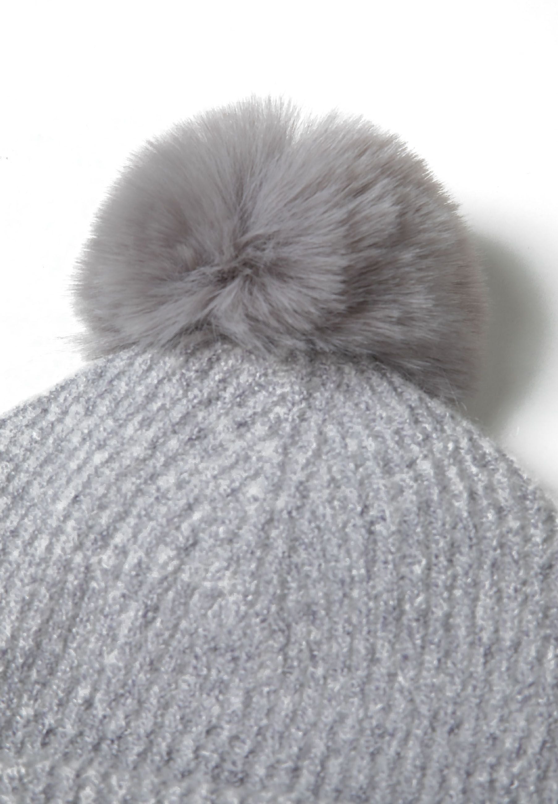 Detail of a grey ribbed knit hat with a metal badge and pompom.