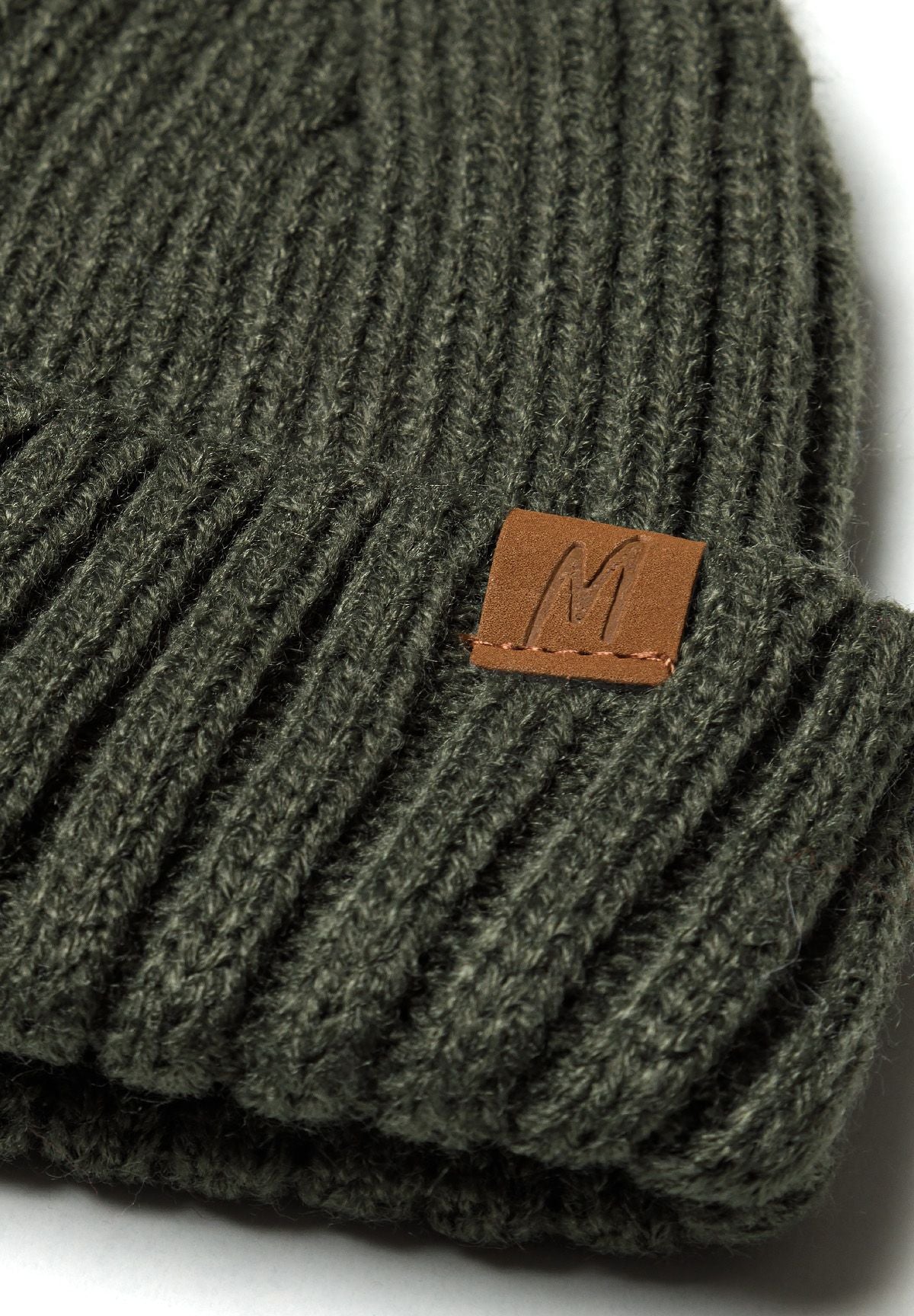 Close-up of tan M logo patch stitched onto olive ribbed hat cuff.