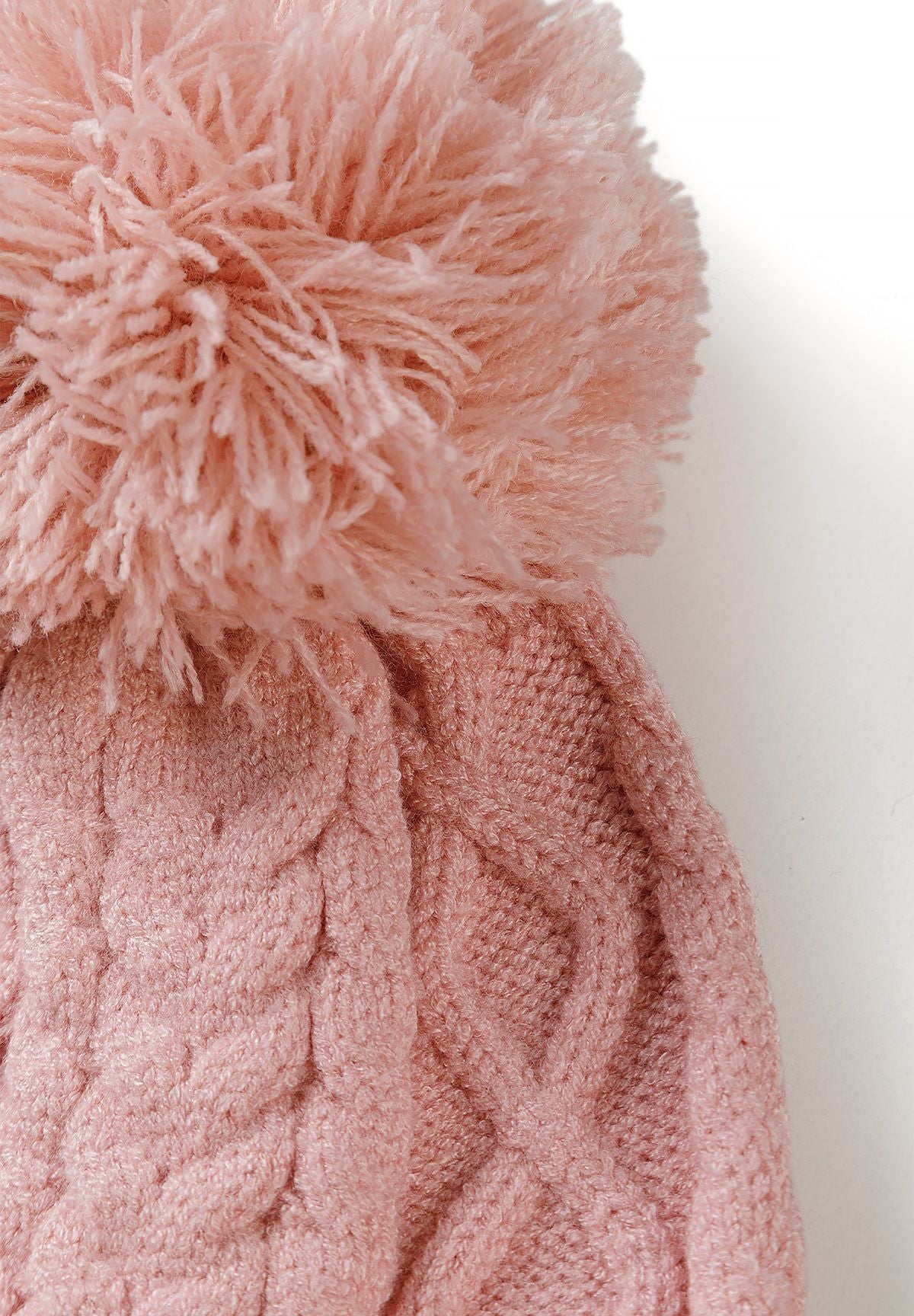 Close-up of the pale pink hat's large yarn pom-pom and raised cable-knit pattern.