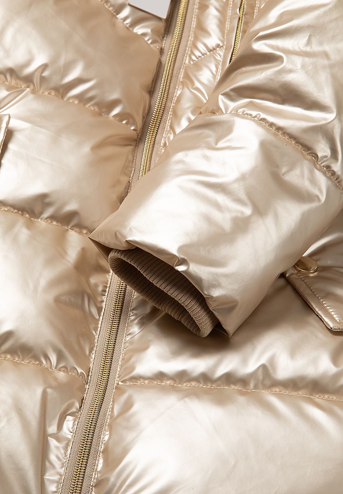 Manteau matelassé doré métallisé pour fille avec capuche en fausse fourrure, gros plan sur les poignets.