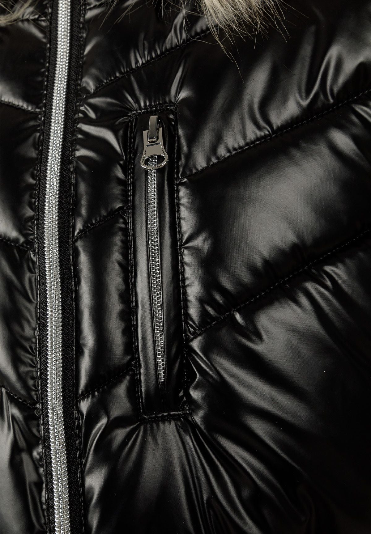 Close-up of the silver front zip and vertical zipped chest pocket on glossy black quilting.