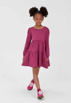 Girl wearing a berry-pink long-sleeved dress with a gathered two-tier skirt.