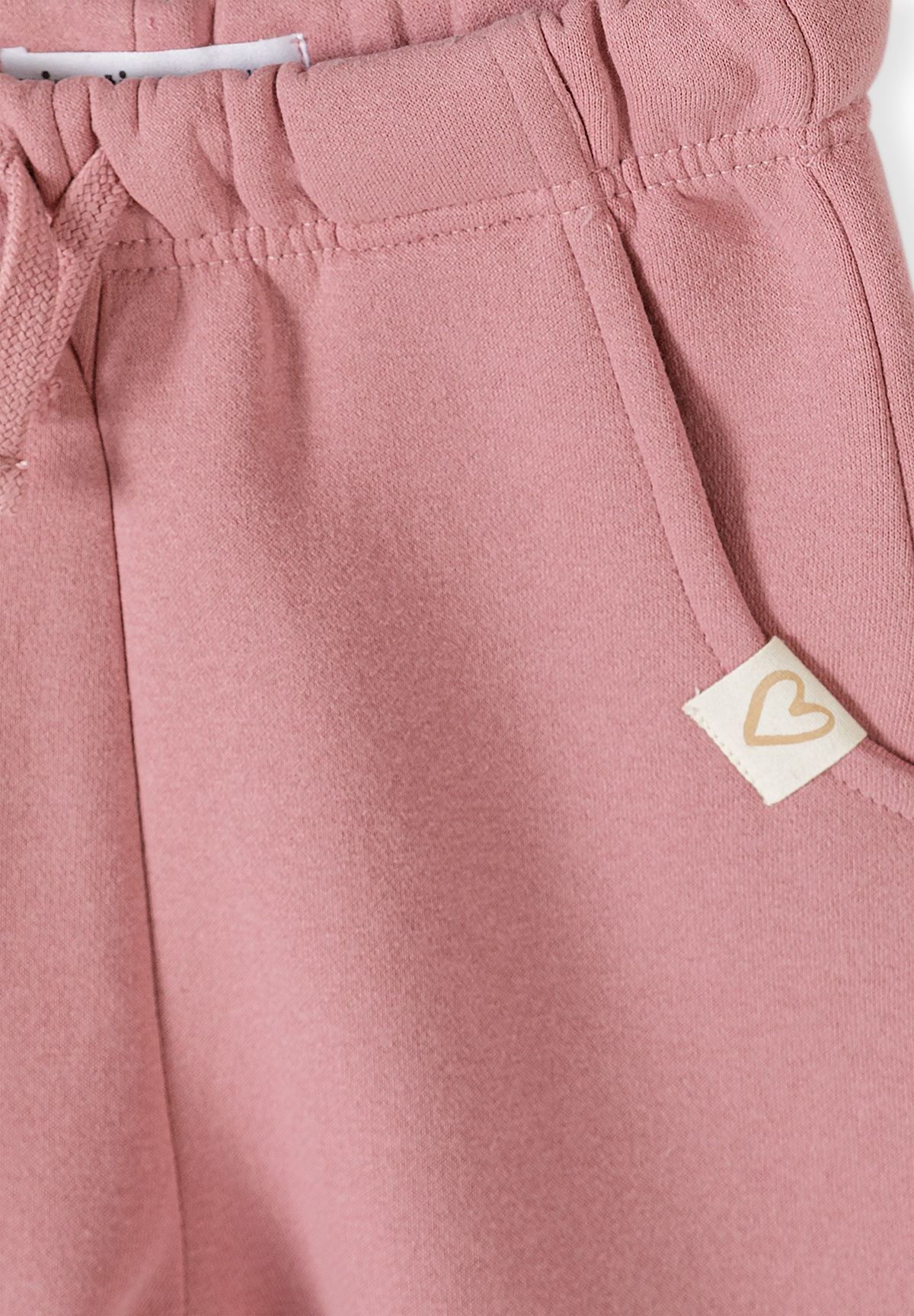 Set composto da felpa rosa con coniglietto e pantaloni a gamba larga da bambina, primo piano della cintura e del distintivo.