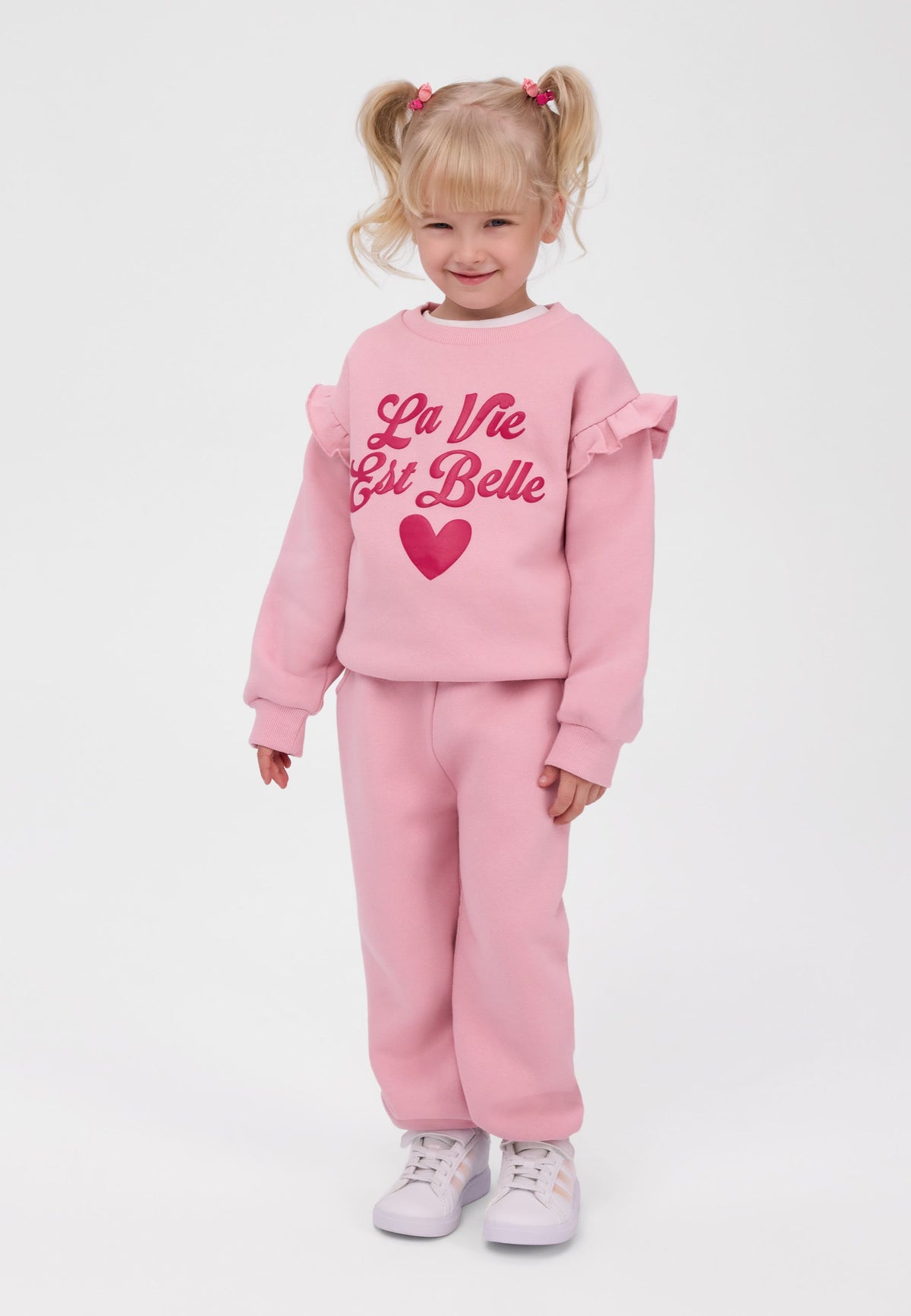 Tuta da ginnastica rosa da bambina con felpa e pantaloni da jogging con bordi a volant, modella vista di fronte.