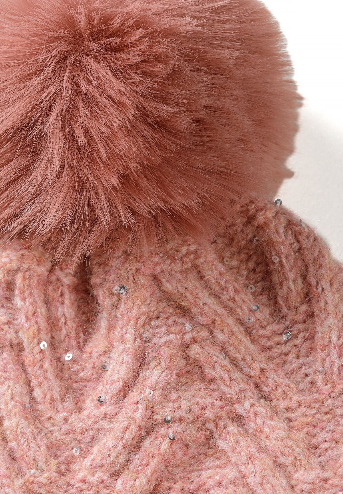 Close-up of dusty pink fluffy hat pompom above chevron knit and silver sequins.