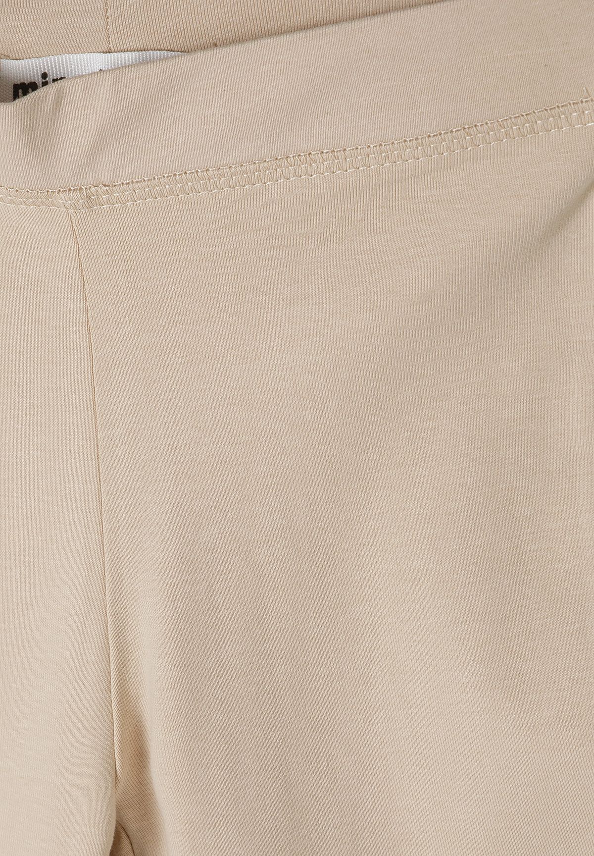 Close-up of sand beige leggings' waistband stitching and fine vertical rib texture.