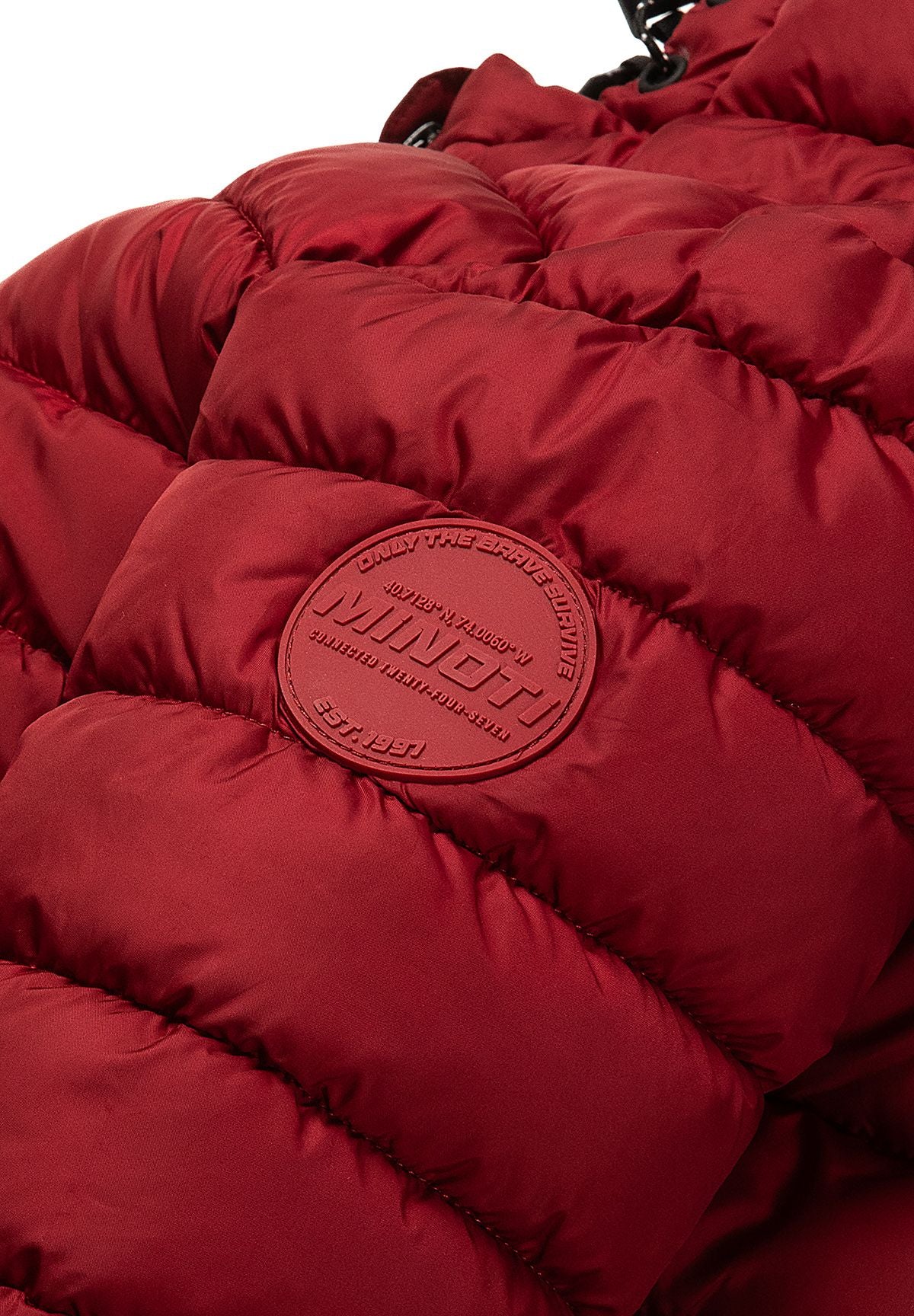 Close-up of a tonal circular Minoti badge on the sleeve of the deep red puffer jacket.