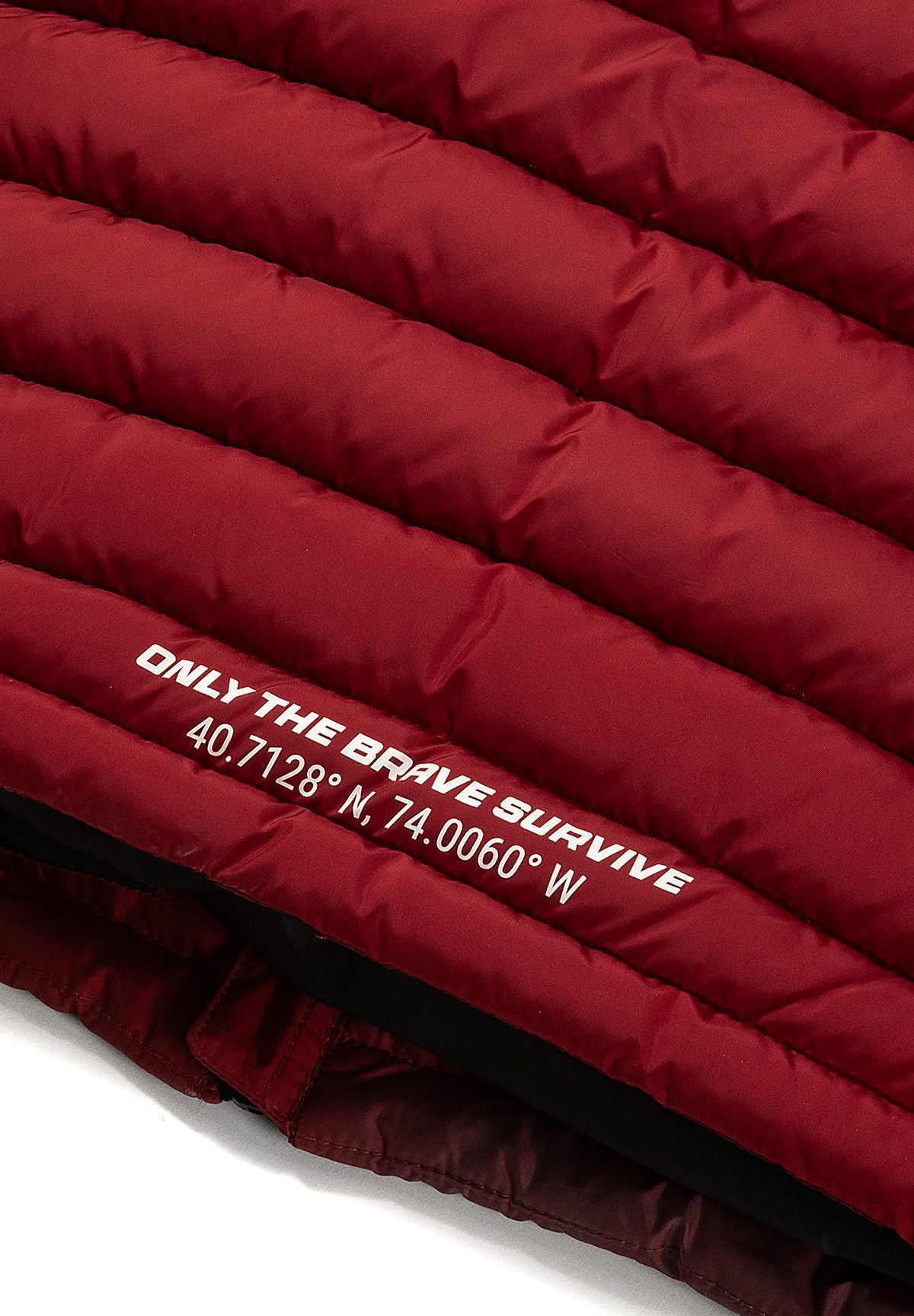 Close-up of the white 'ONLY THE BRAVE SURVIVE' slogan and coordinates on the red back hem.