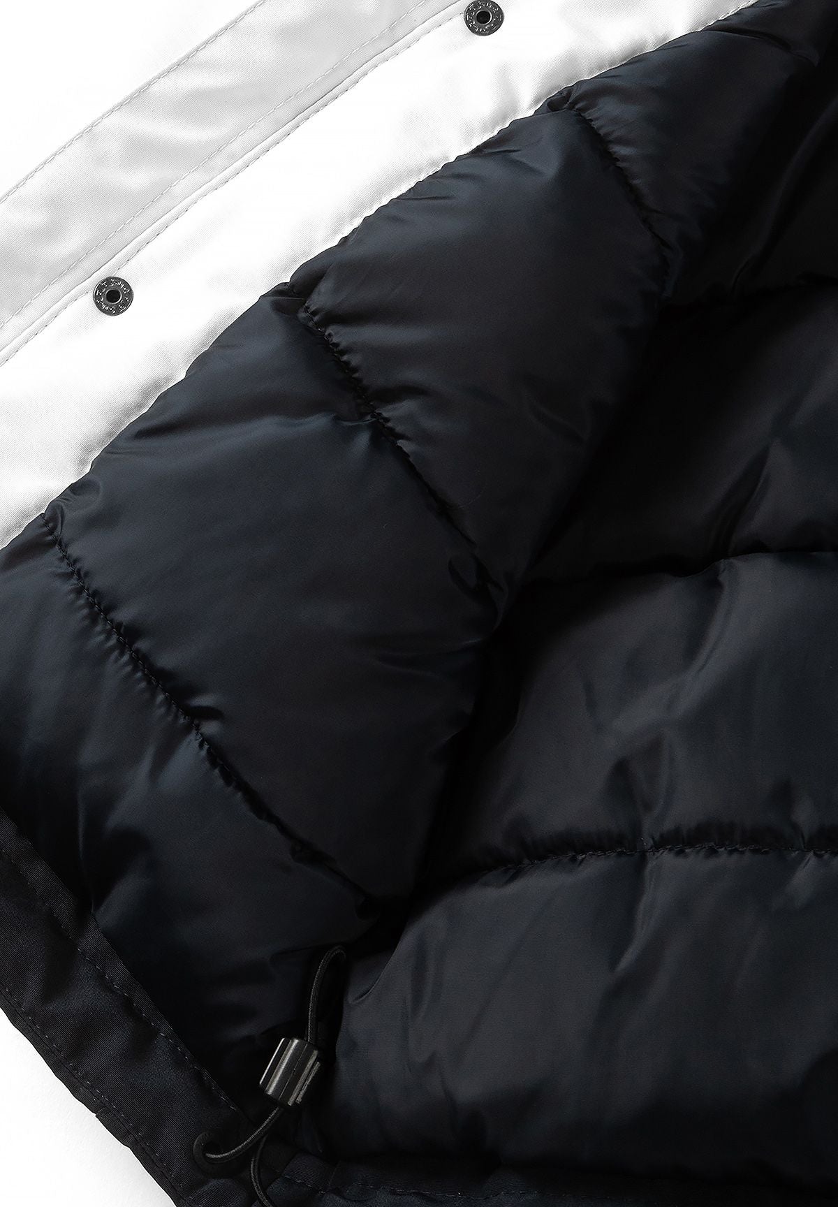 Inside of the parka showing dark quilted lining beside a cream snap-fastened placket.