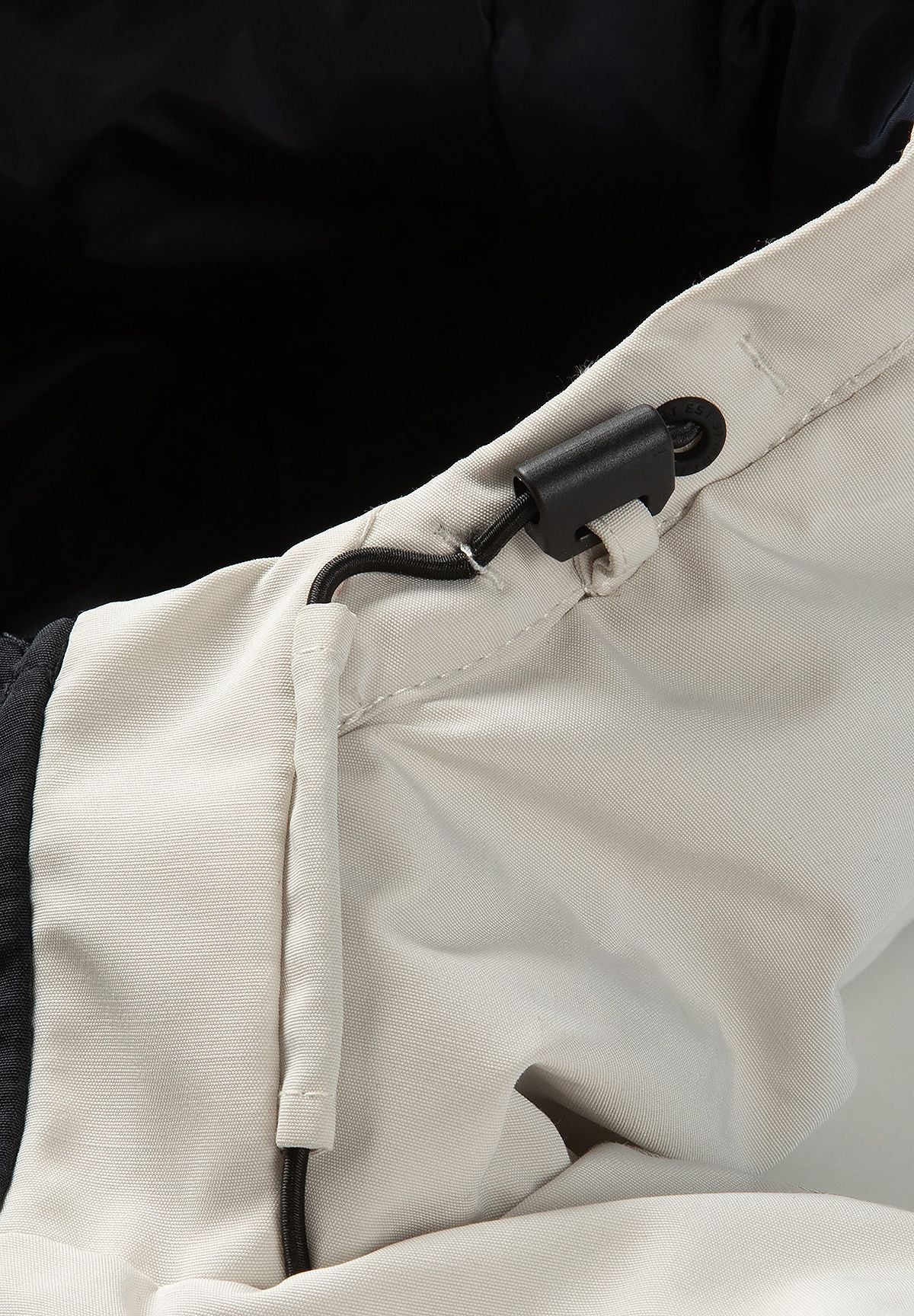 Close-up of the cream parka hood with a black drawcord, eyelet and sliding adjuster.