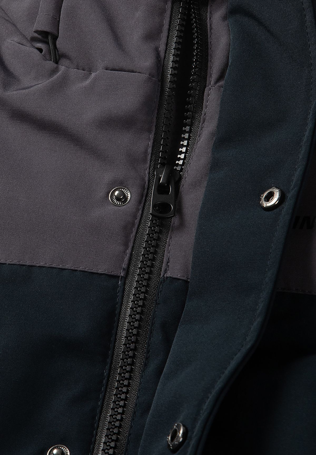 Close-up of the parka's black centre zip beneath a charcoal storm flap with metal snaps.