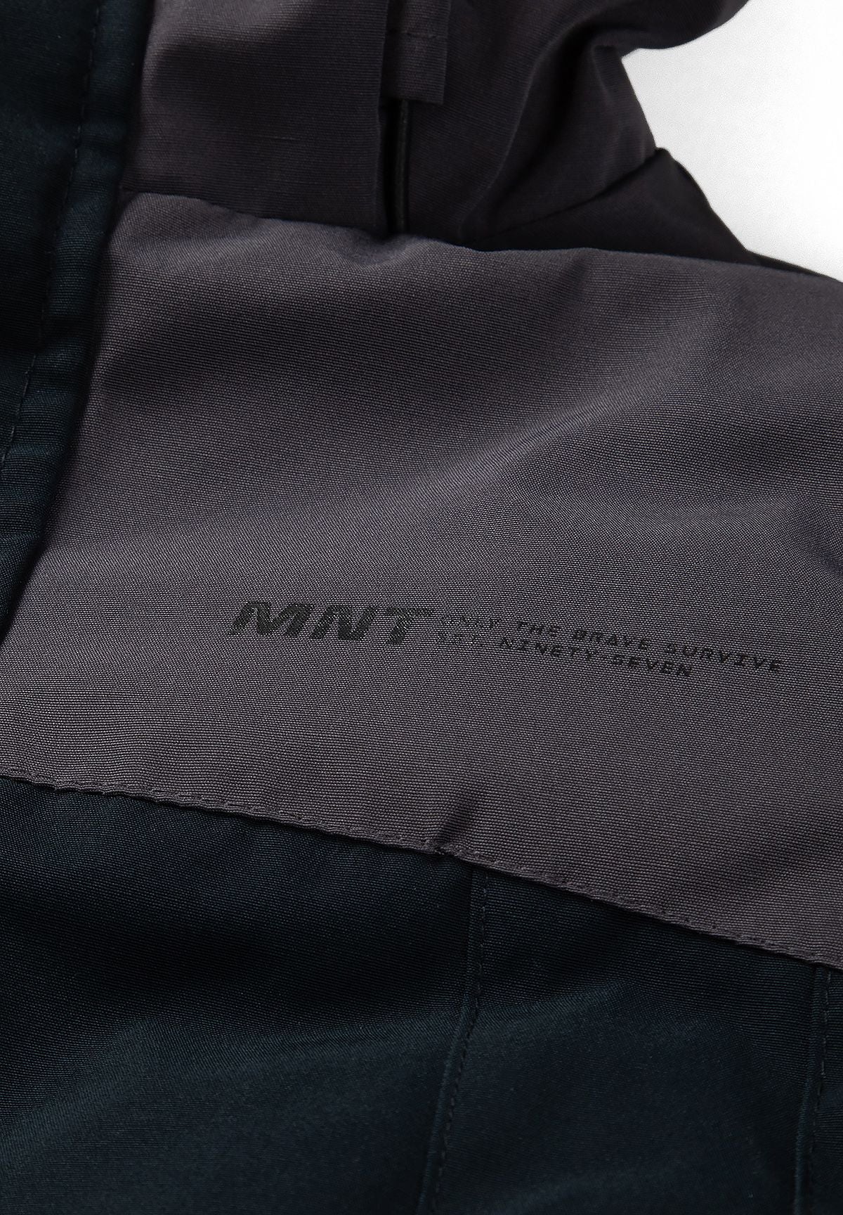 Detail of the small tonal MNT chest print on the parka's charcoal upper panel.