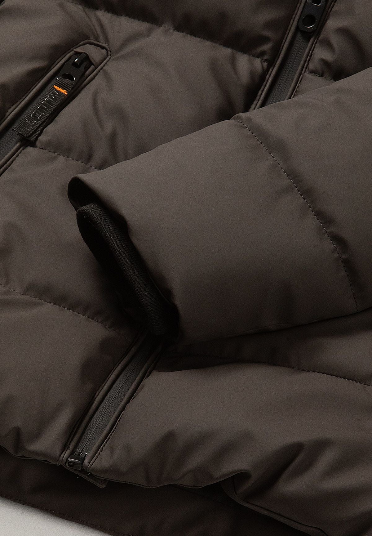 Brown padded sleeve with a narrow black inner cuff beside one of the long zipped pockets.