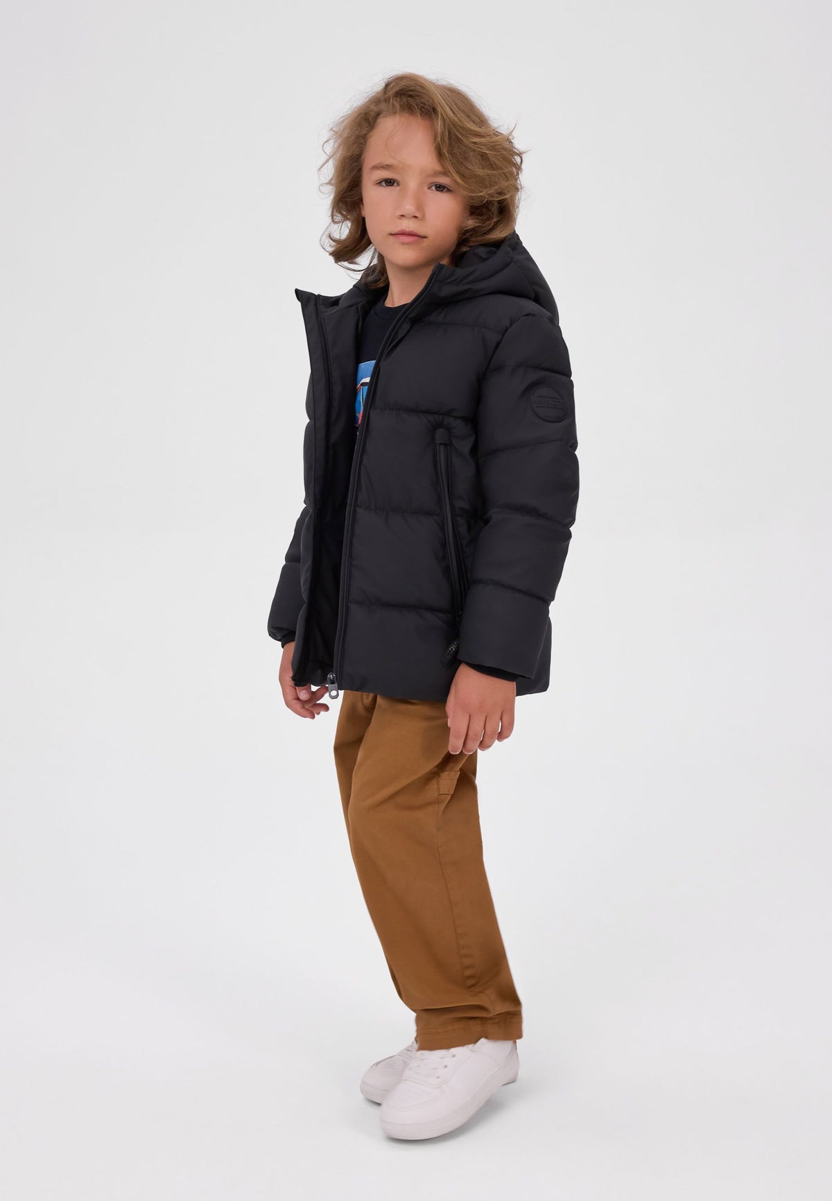 Boy in a matte black hooded puffer jacket with an open front zip, vertical zipped pockets and sleeve badge.