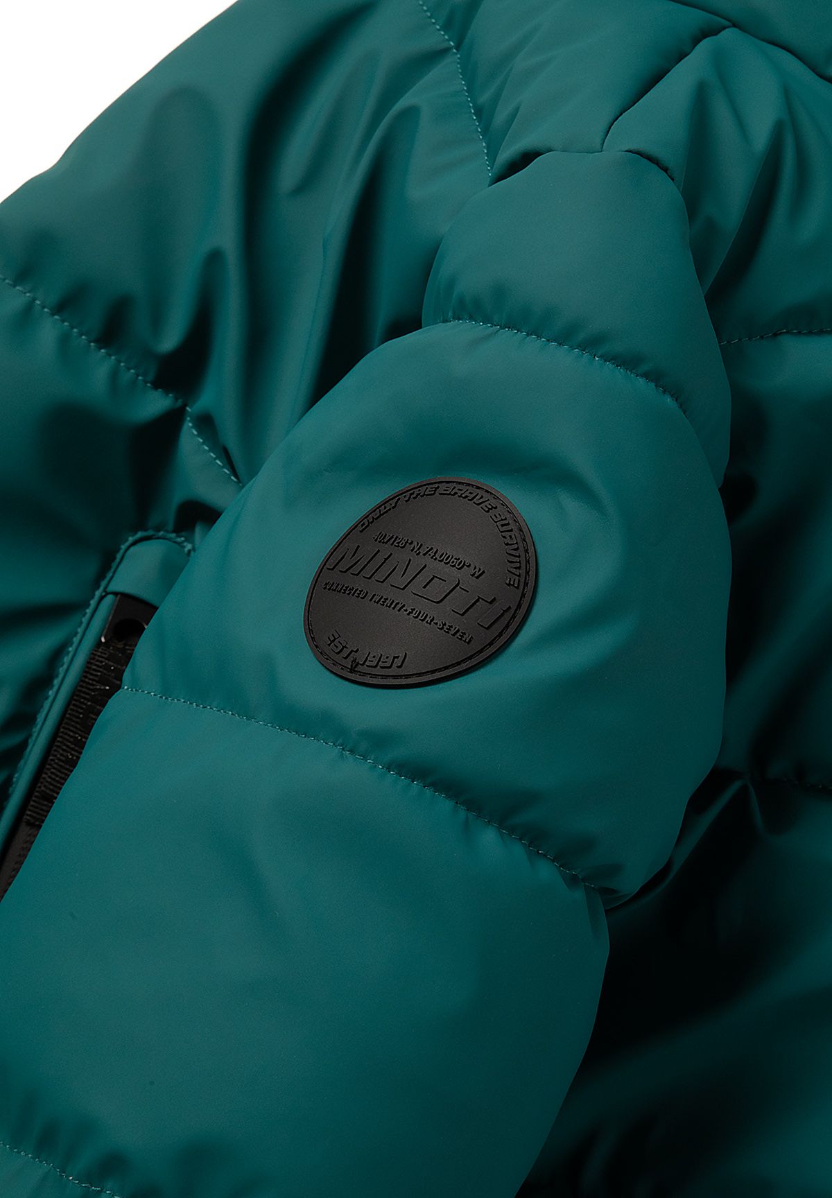 Close-up of a round dark embossed badge on the teal puffer jacket's upper sleeve.