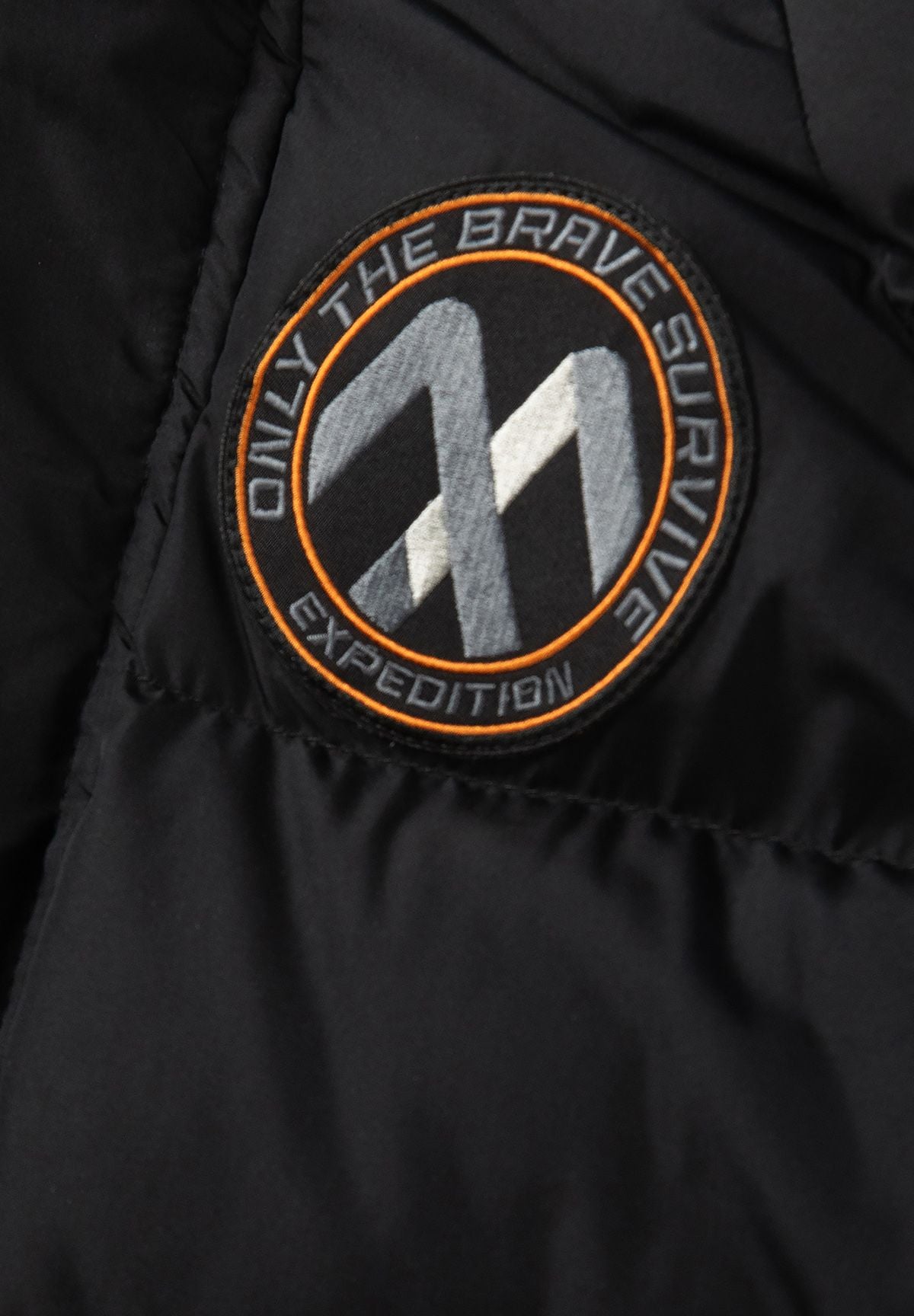 Zwarte gewatteerde parka voor jongens met afneembare capuchonrand, detail van het embleem op de mouw.