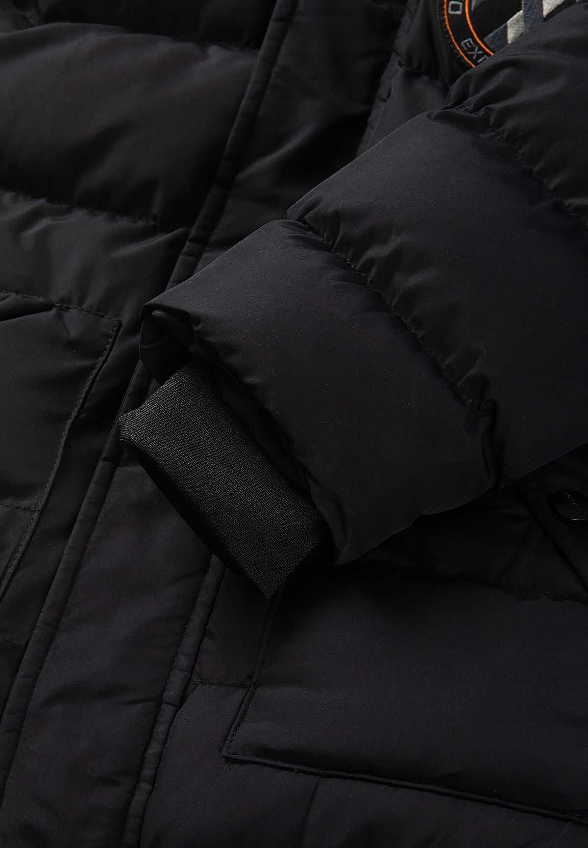 Zwarte gewatteerde parka voor jongens met afneembare capuchonrand, detail van de mouw.
