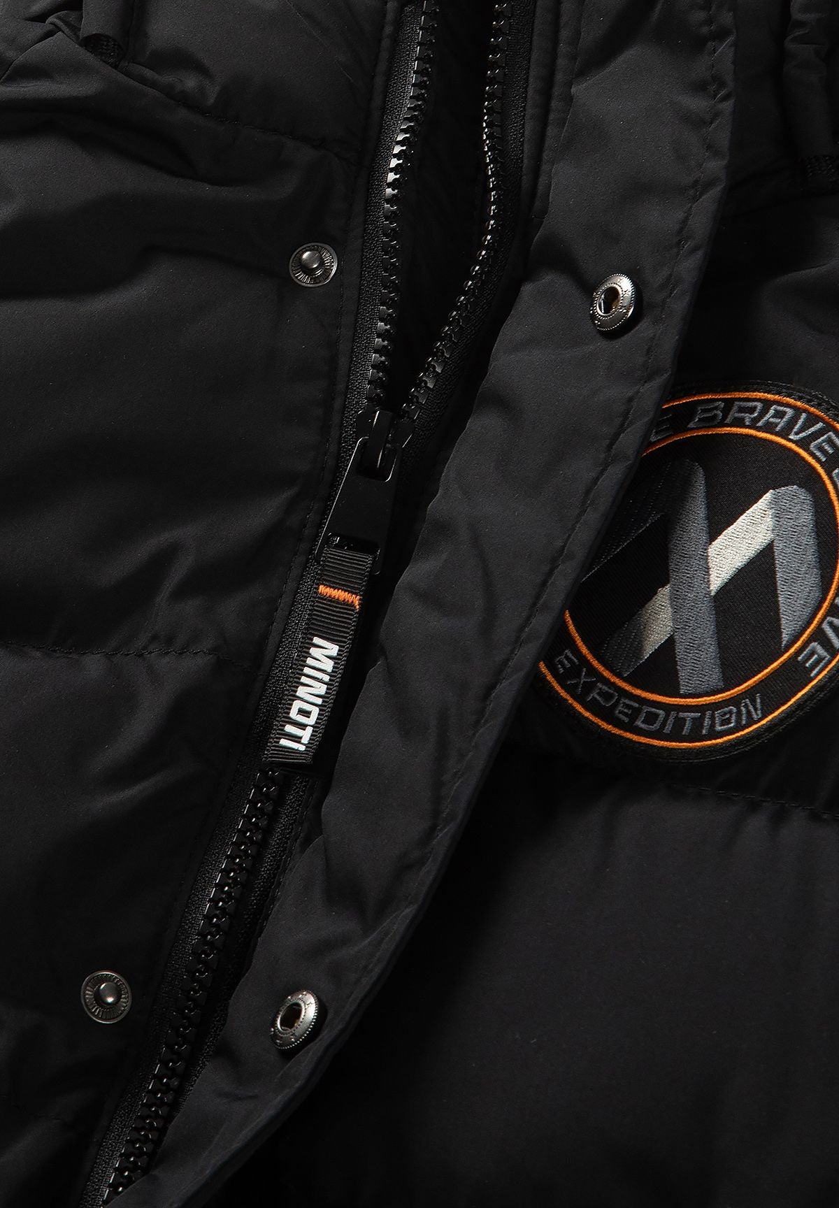 Zwarte gewatteerde parka voor jongens met afneembare capuchonrand, detail van de rits, drukknopen en badge.