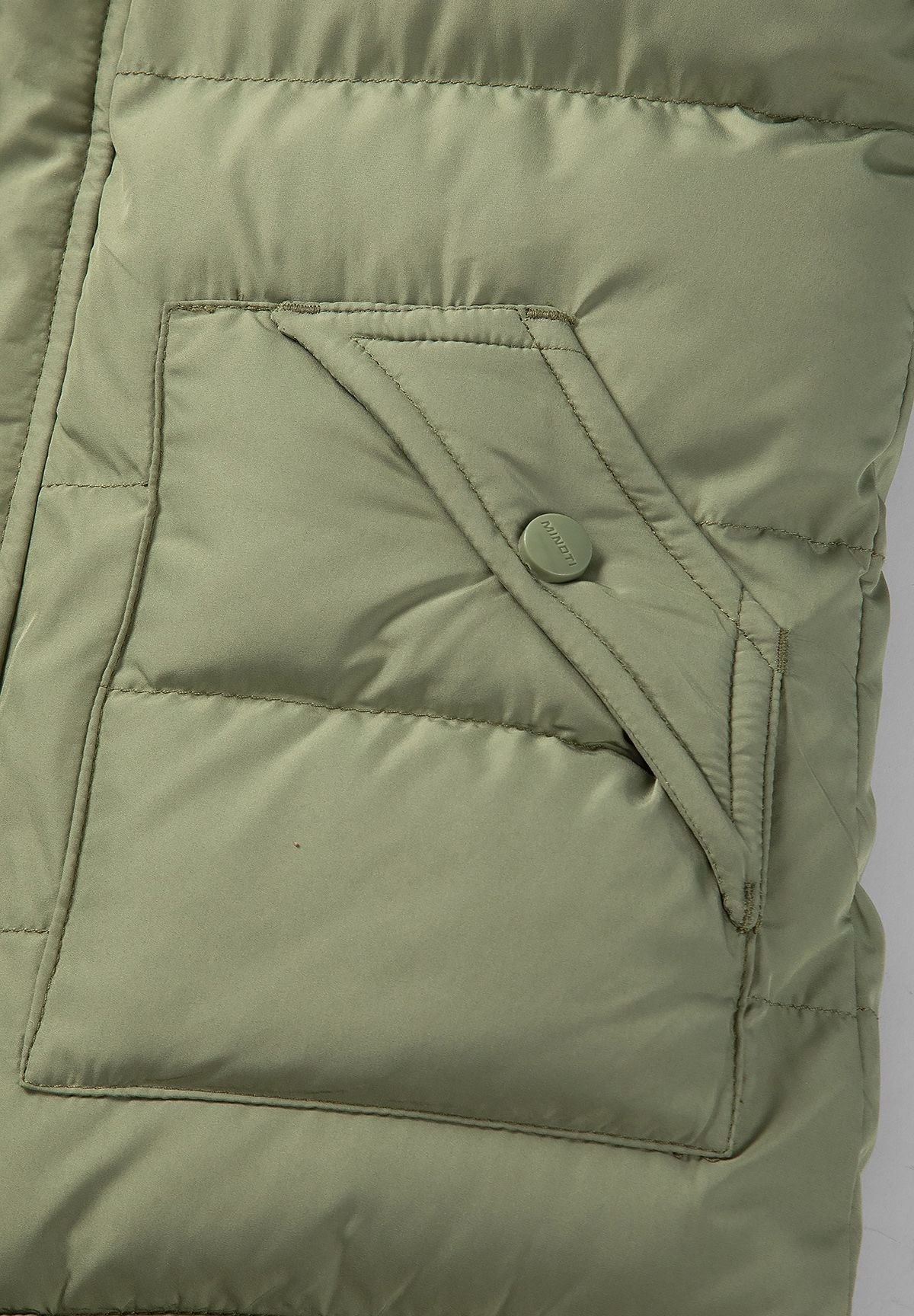 Parka acolchada de color oliva para niño con ribete de la capucha desmontable; primer plano del bolsillo con solapa.