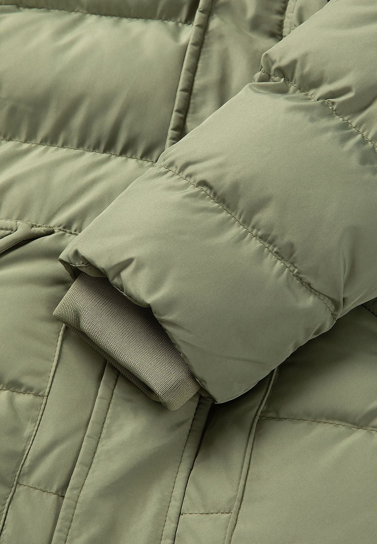 Parka acolchada de color oliva para niño con ribete de la capucha desmontable; primer plano del puño.