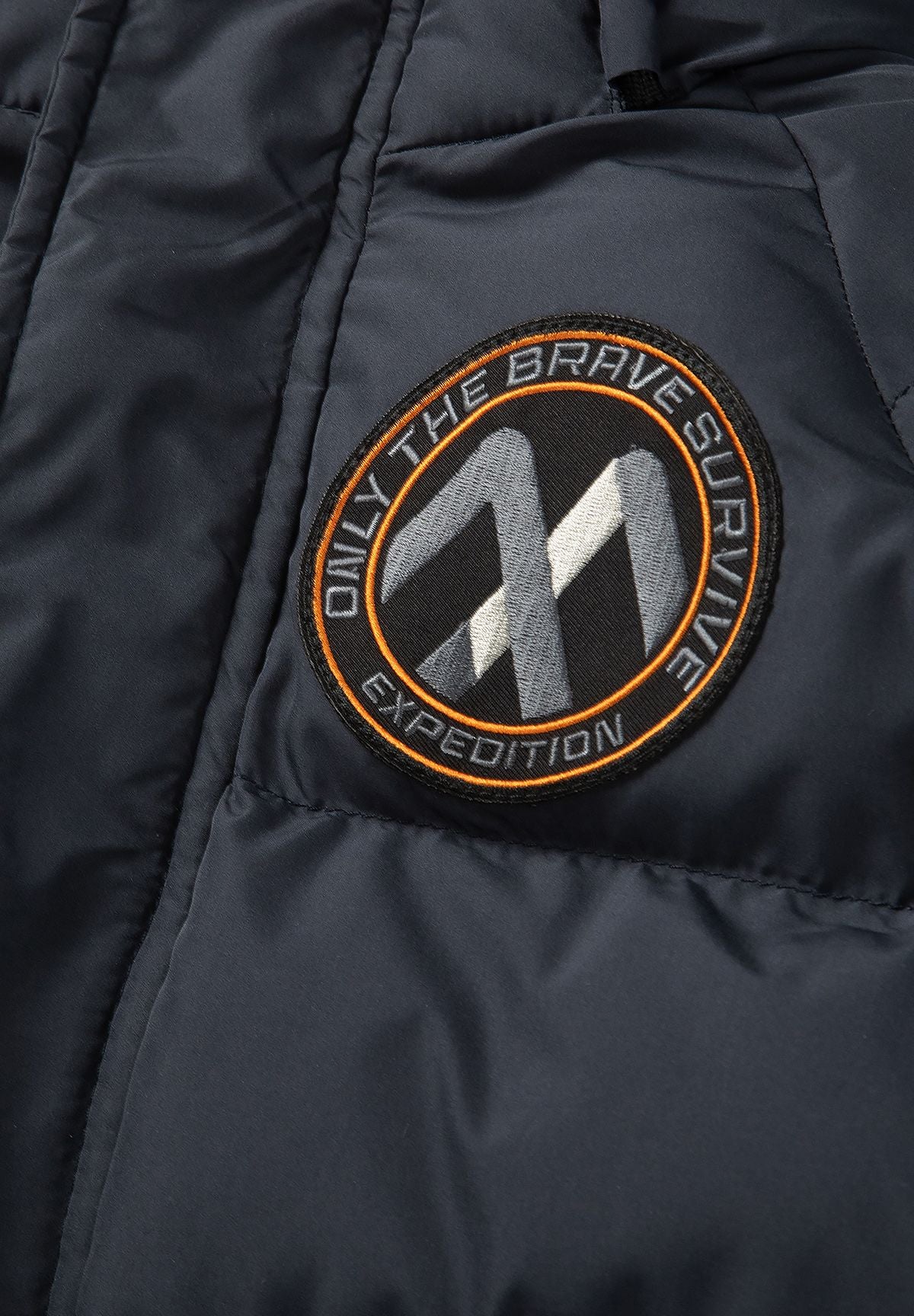 Donkerblauwe gewatteerde parka voor jongens met afneembare capuchonrand, detail van het embleem op de mouw.