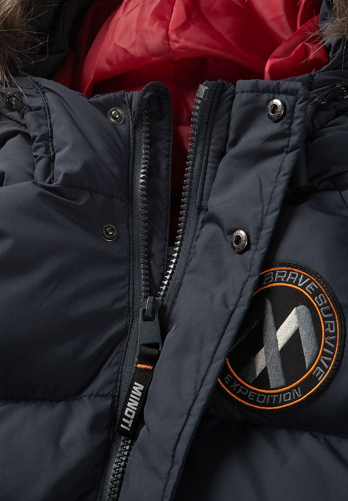 Donkerblauwe gewatteerde parka voor jongens met afneembare capuchonrand, detail van de rits, drukknopen en badge.