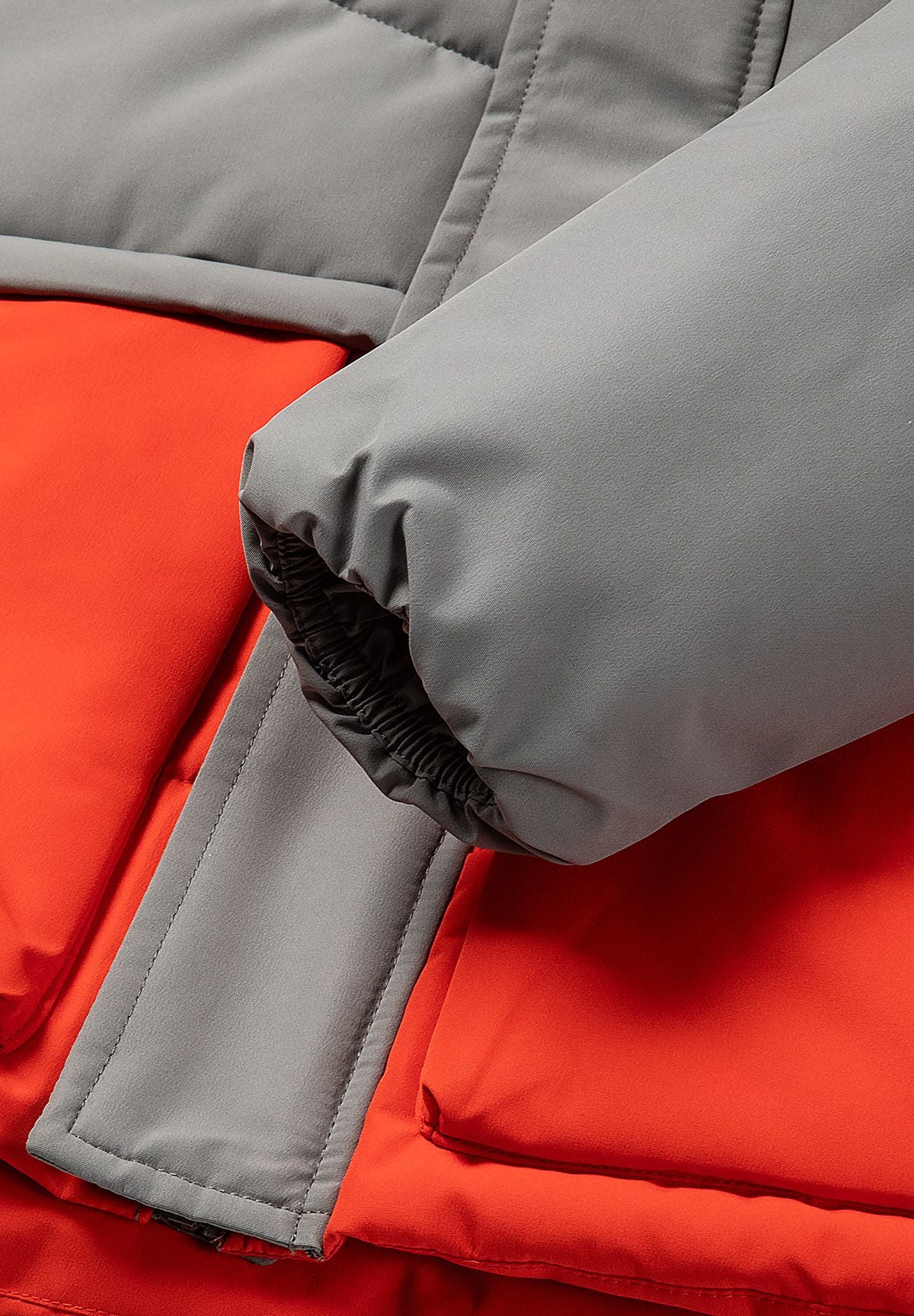 Grijze en rode gewatteerde parka met kleurblokken voor jongens, detail van het lipje aan de manchet.