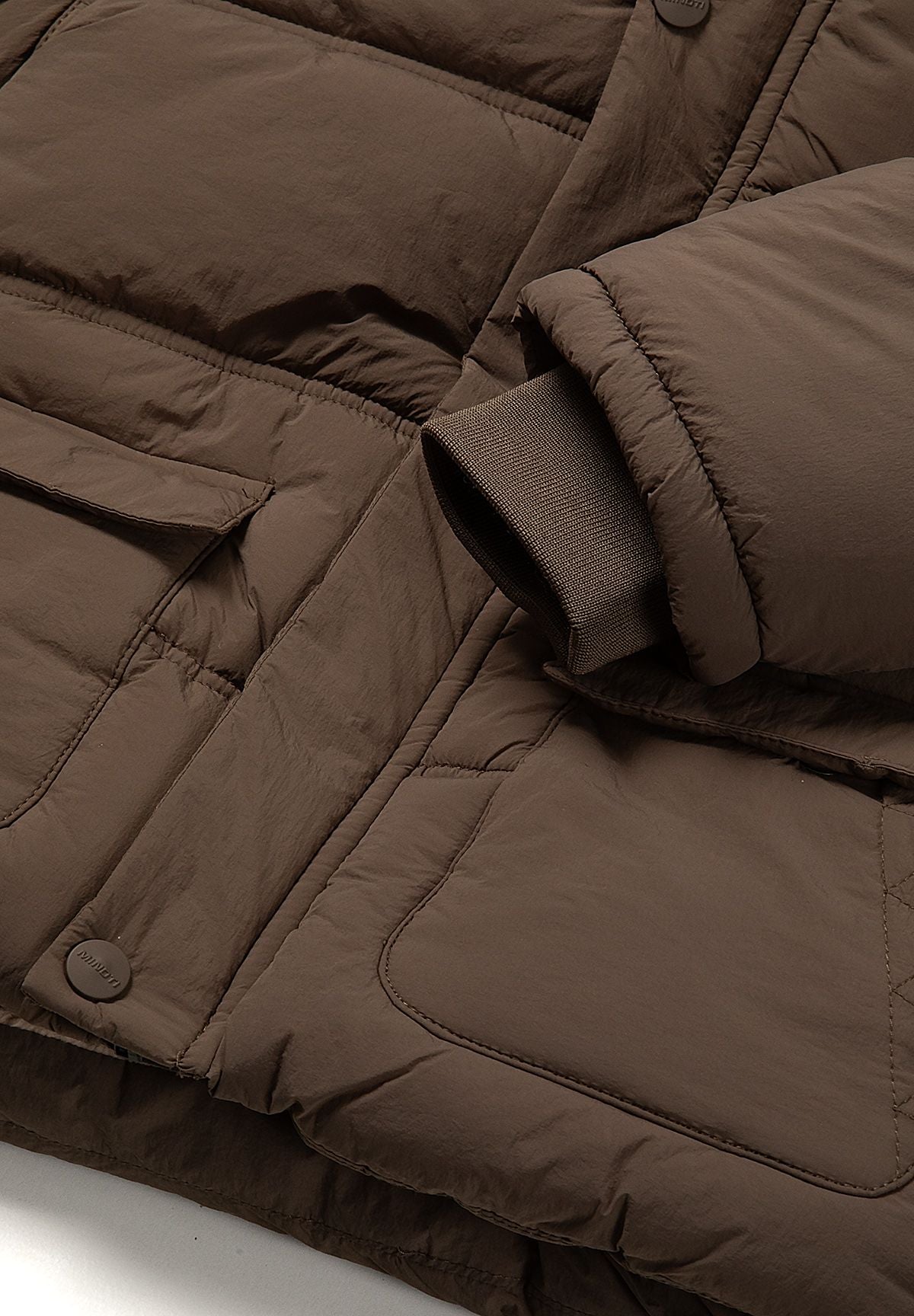 Close-up of a lower flap pocket and rib-knit sleeve cuff on the brown padded jacket.