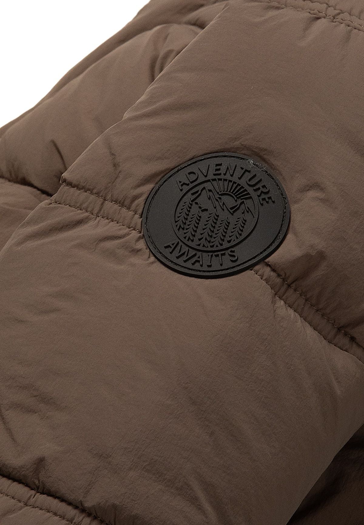 Close-up of a black circular 'Adventure Awaits' badge on the brown jacket sleeve.