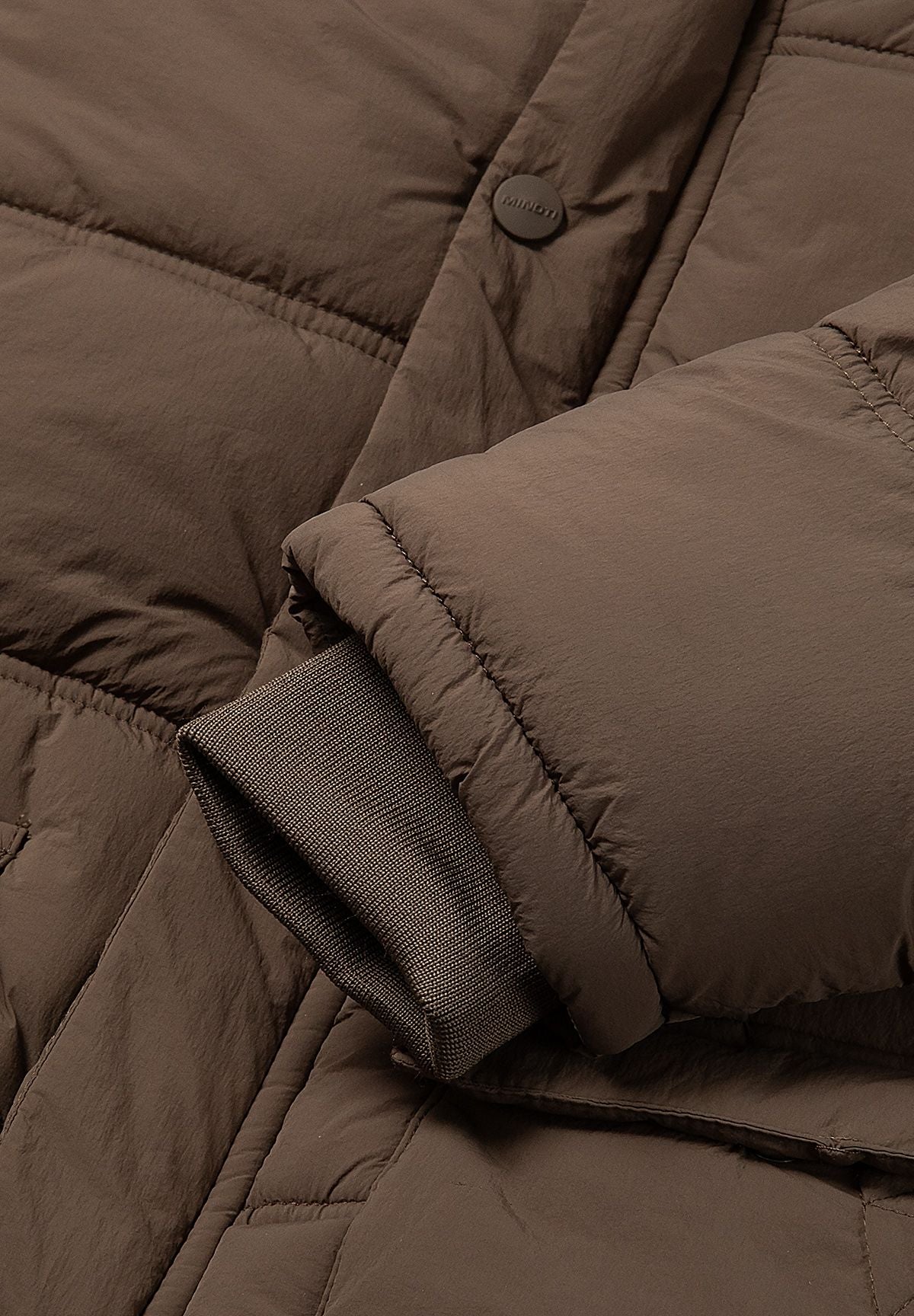 Close-up of the dark brown rib-knit cuff beneath the padded sleeve of the jacket.