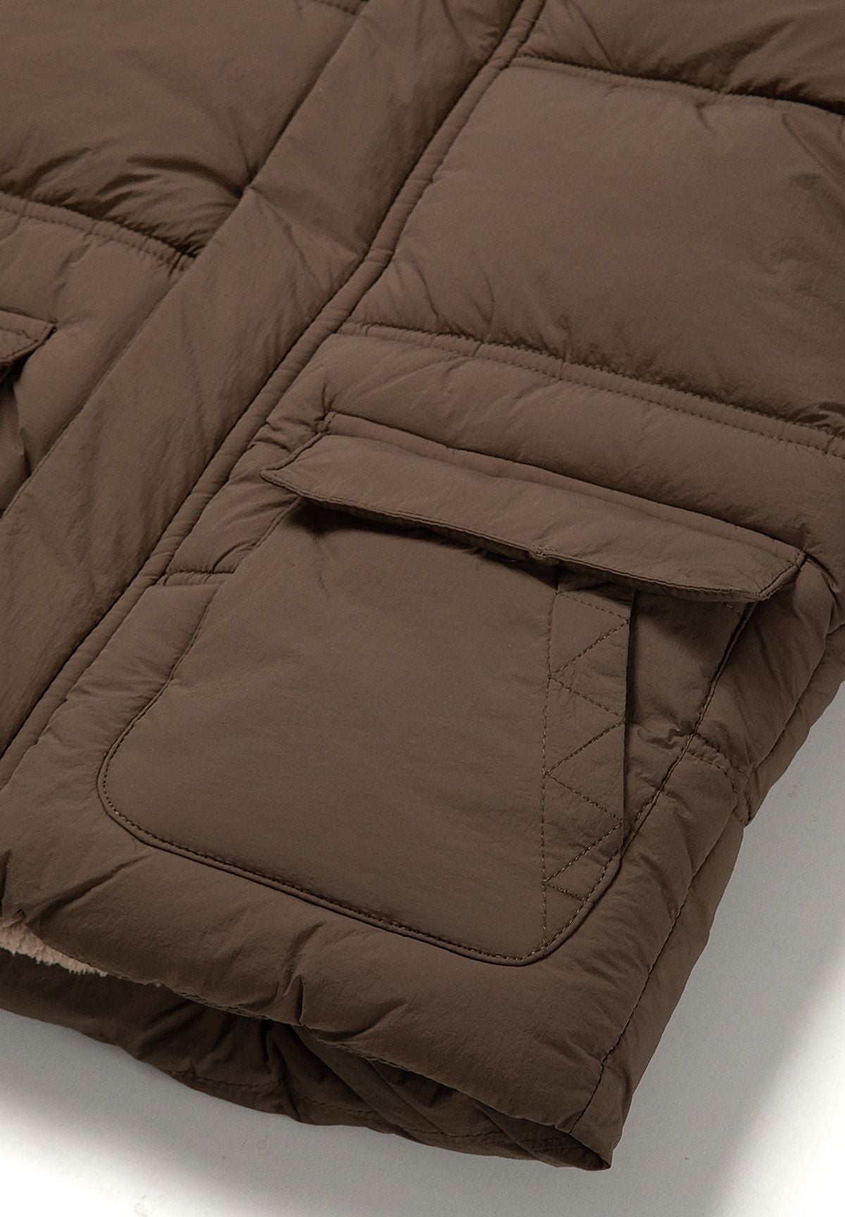 Close-up of a large lower patch pocket with a broad flap on the brown padded jacket.