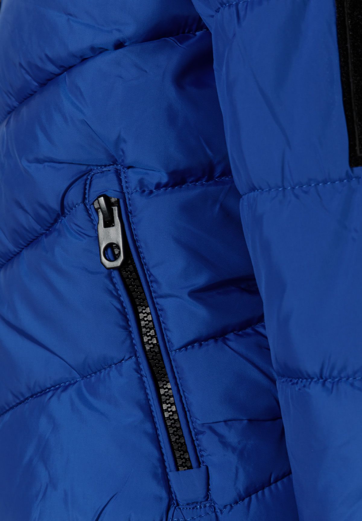 Blauwe pufferjas met capuchon voor jongens, met ritszakken, detail van de zijzak met ritssluiting.
