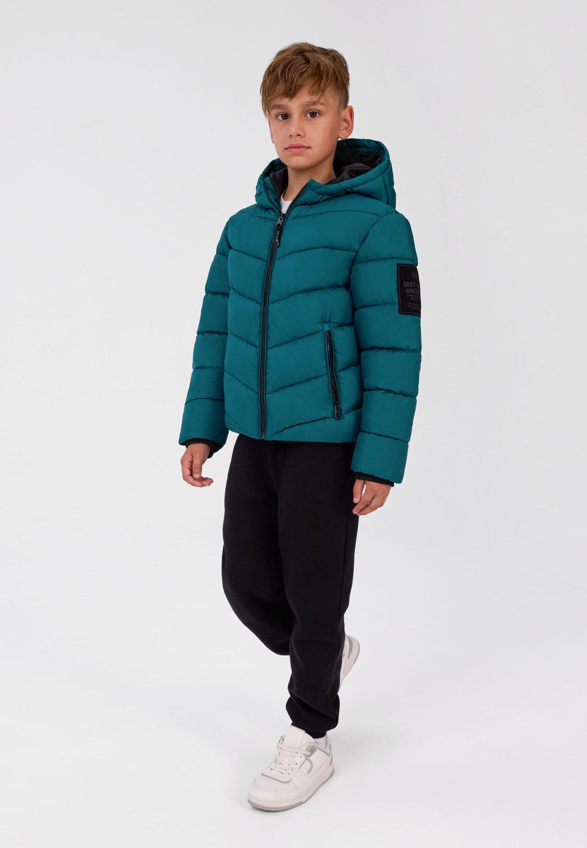 Boy wearing a teal-green hooded puffer with angled quilting, black zip pockets and sleeve badge.