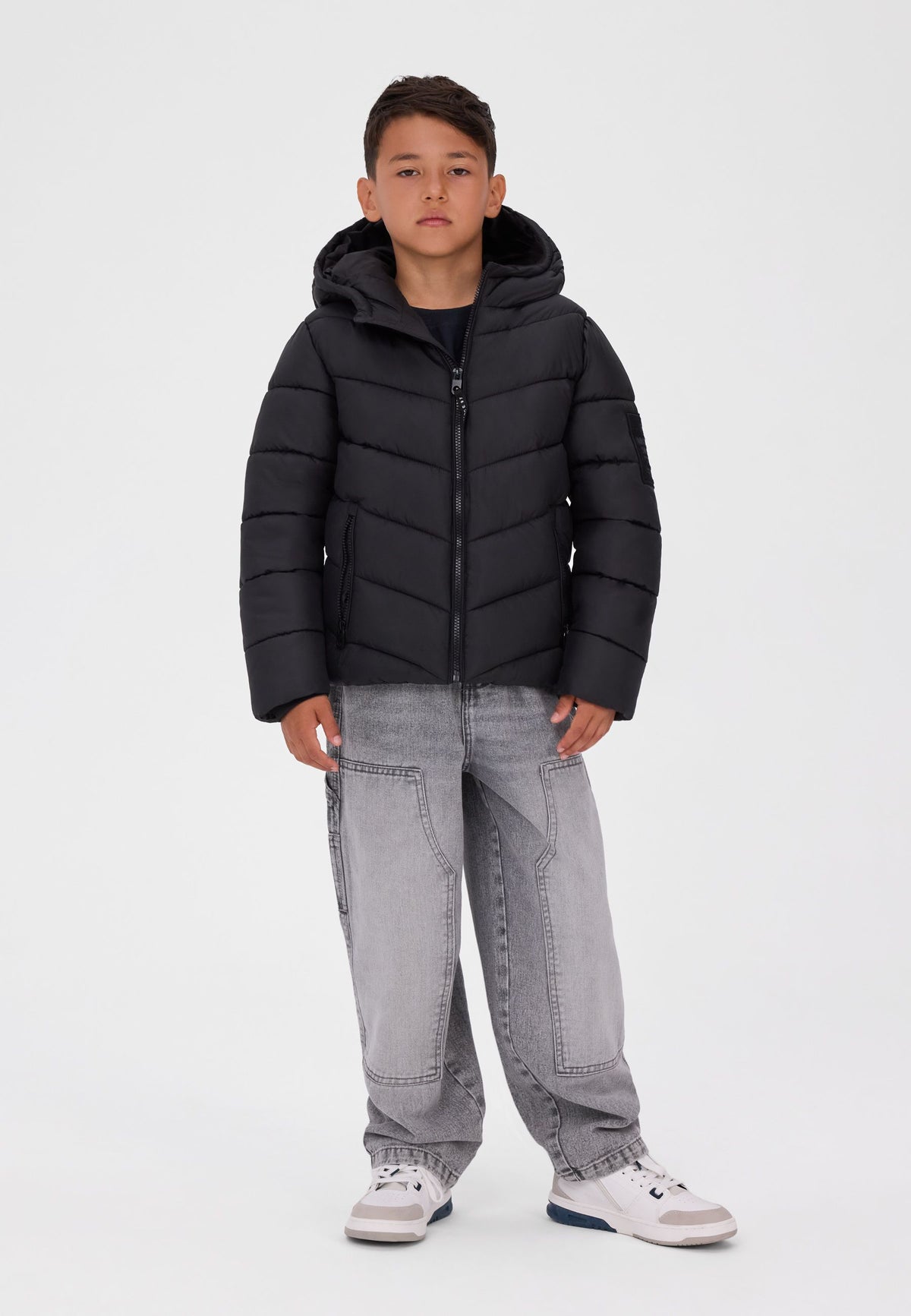 Boy wearing a black hooded puffer jacket with angled front quilting and two zipped pockets.