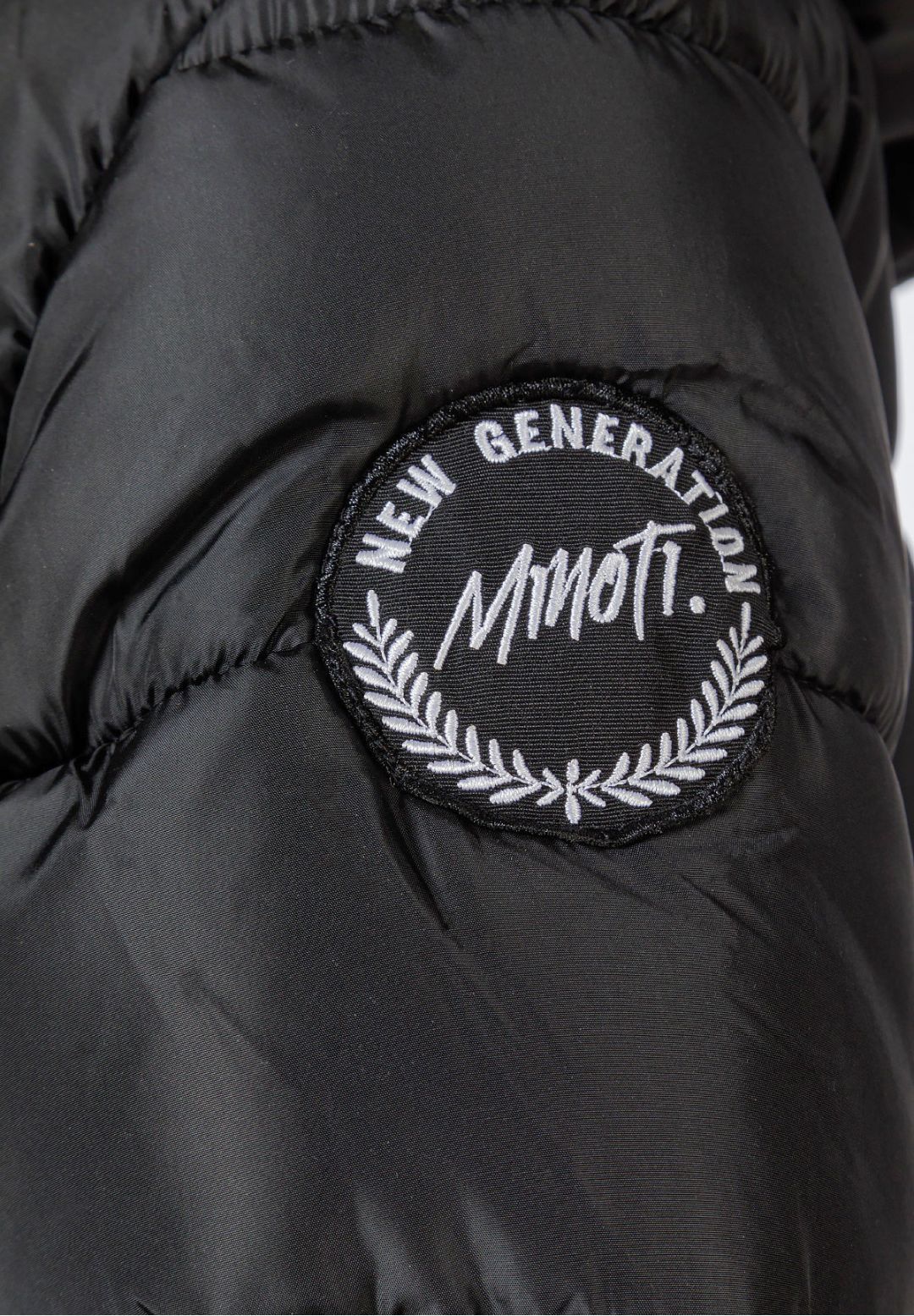 Close-up of a round black Minoti New Generation badge on the charcoal coat sleeve.