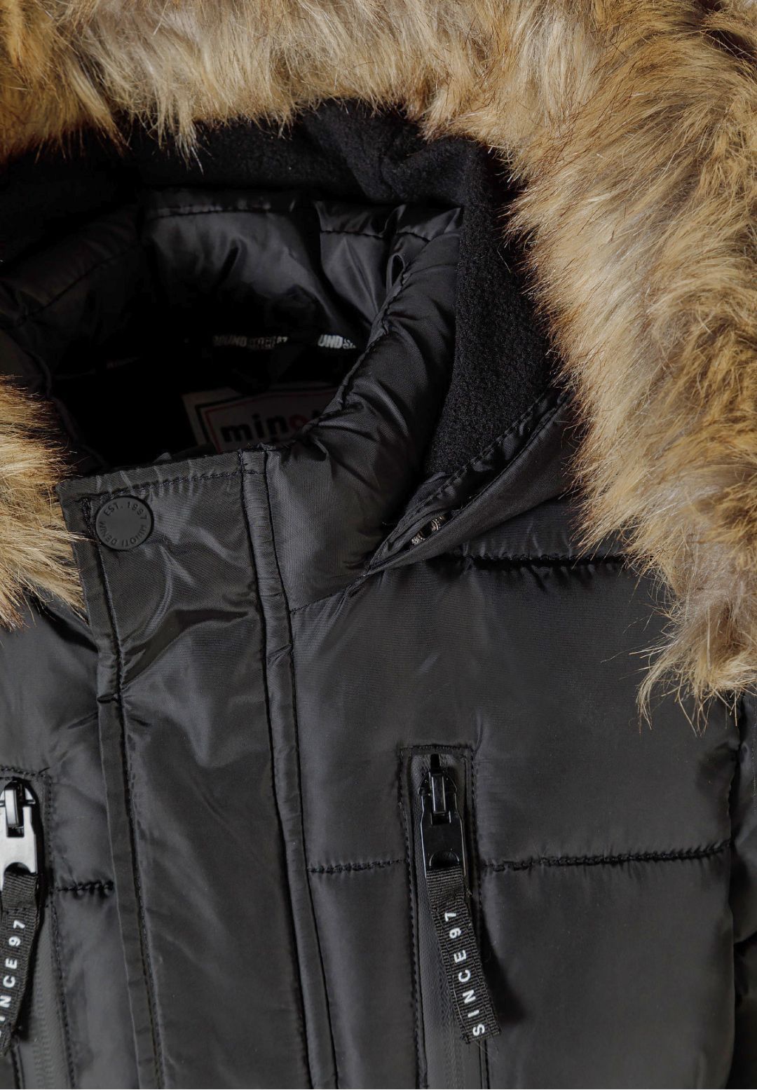 Close-up of tan-brown fluffy hood trim and black inner lining above the charcoal parka's chest zips.