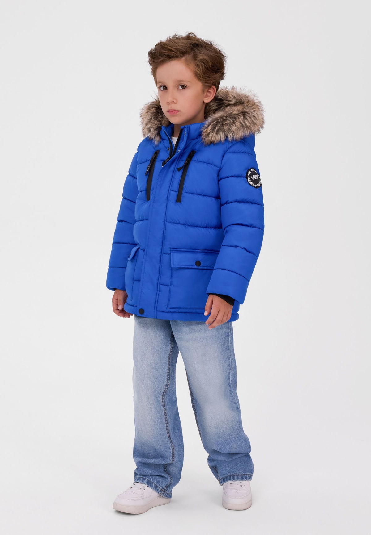 Boy wearing a royal blue quilted parka with fur-look hood, twin chest zips and lower flap pockets.