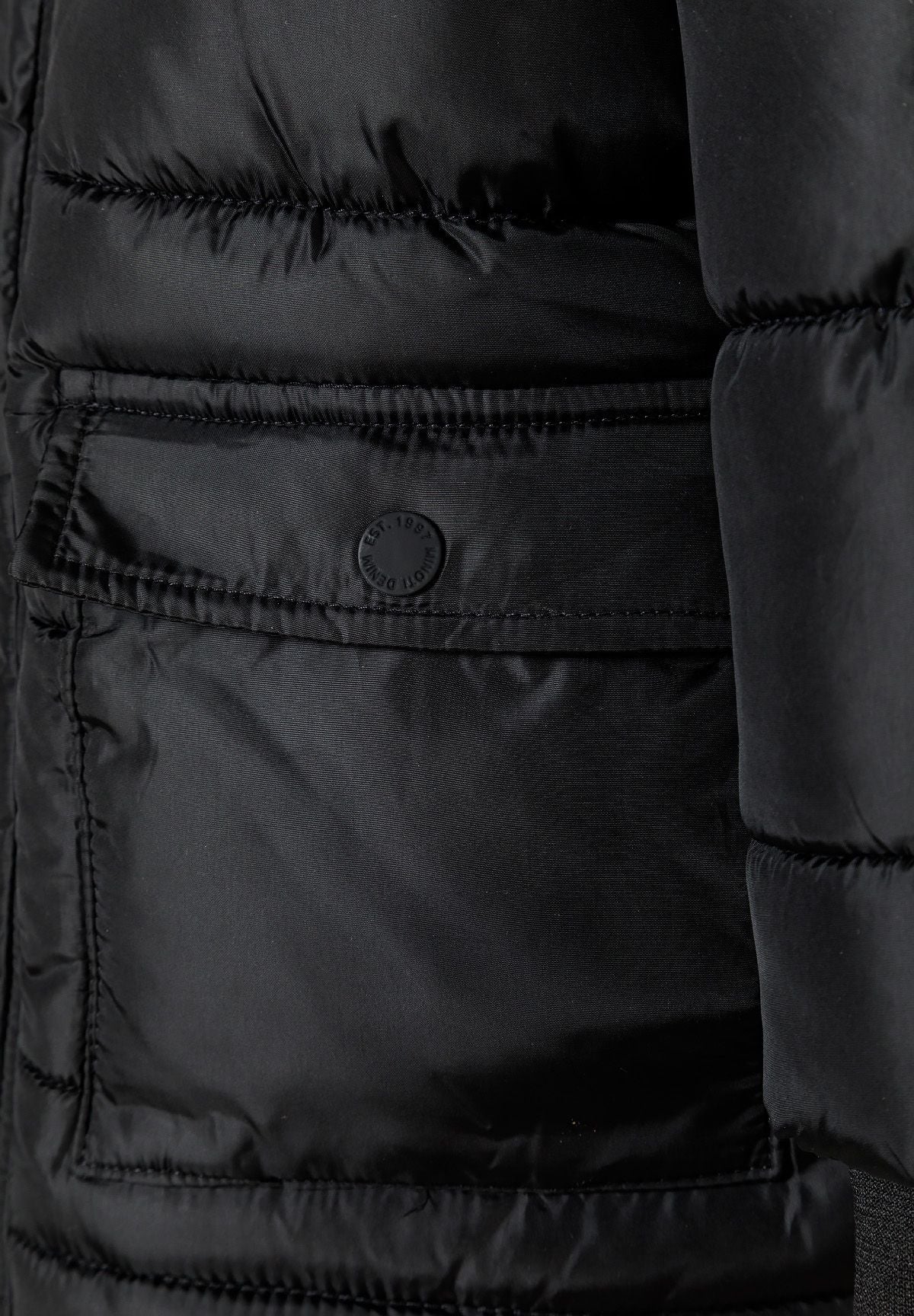 Close-up of a black rectangular parka pocket with a flap and round snap button.