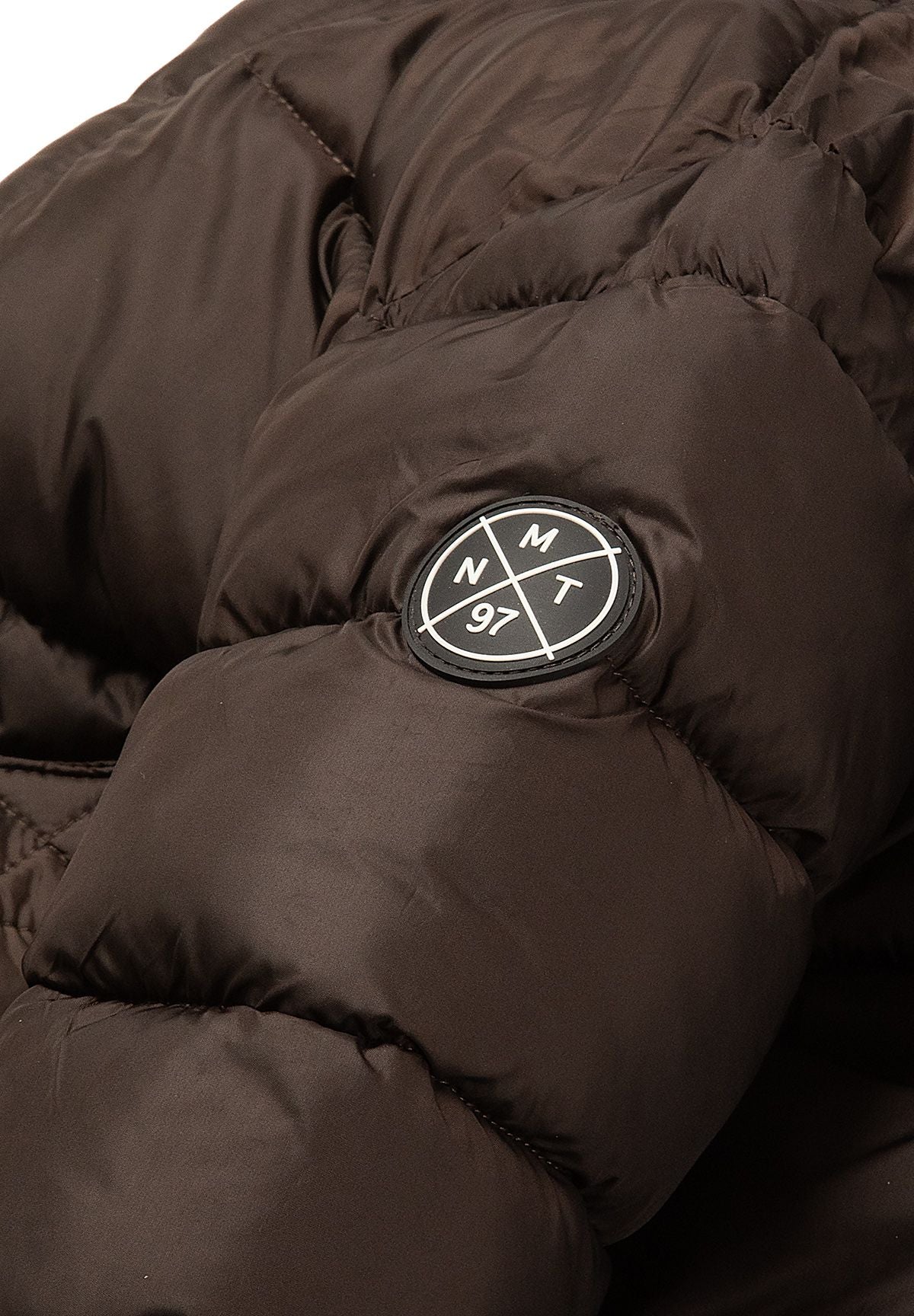 Round black and white Minoti 97 badge on the quilted sleeve of the brown coat.