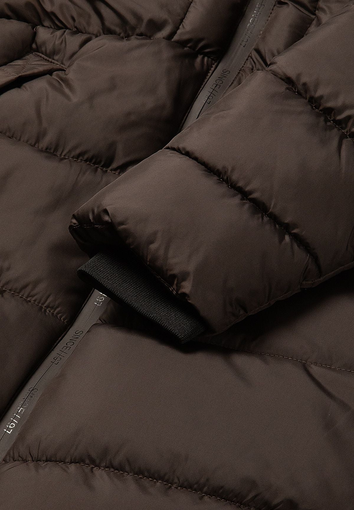 Black ribbed inner cuff beneath the wide padded sleeve of the brown puffer coat.