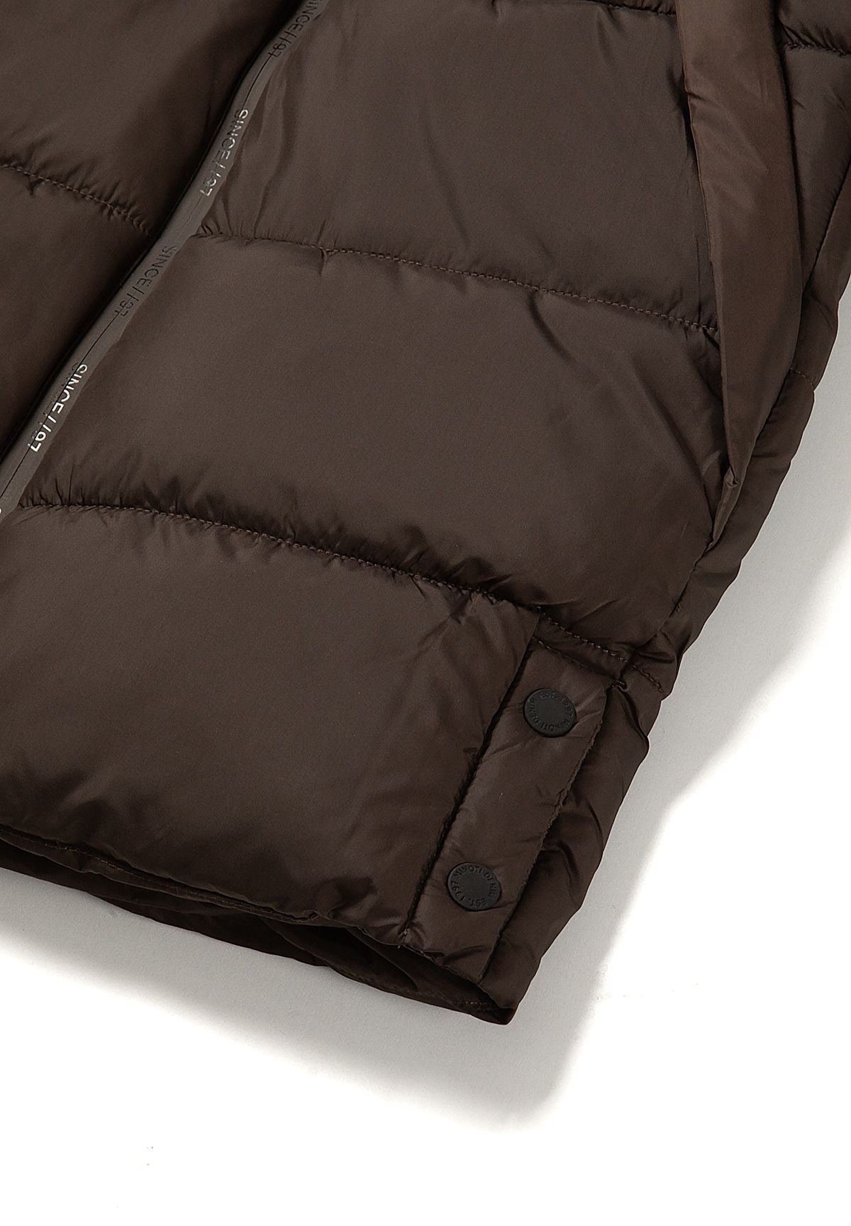 Two black snap fasteners on the brown puffer coat's lower side opening.