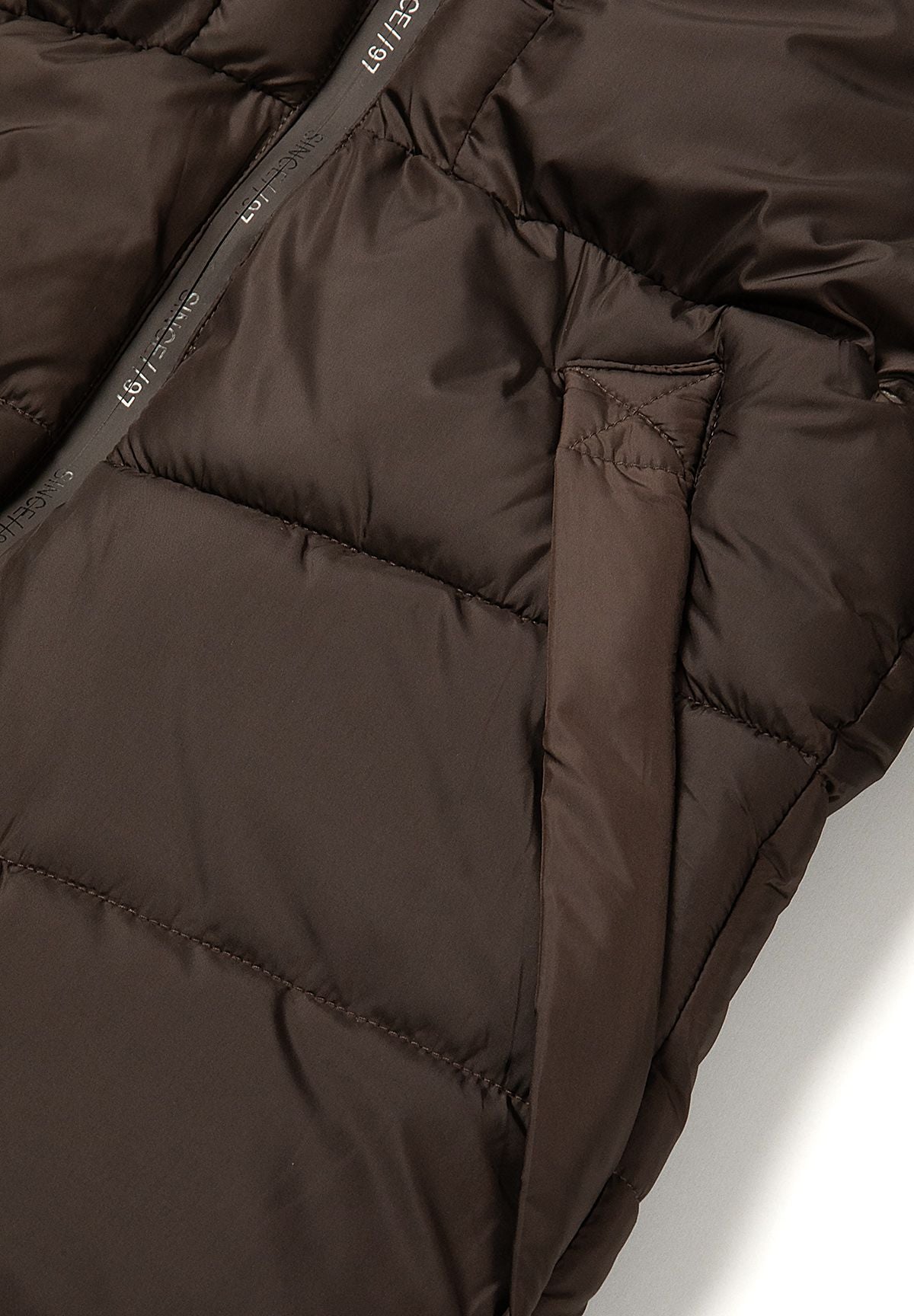 Angled side pocket opening on the dark brown quilted puffer coat.