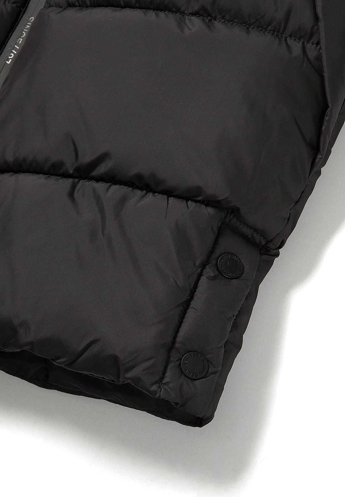 Close-up of two round side hem poppers on the dark charcoal padded coat.