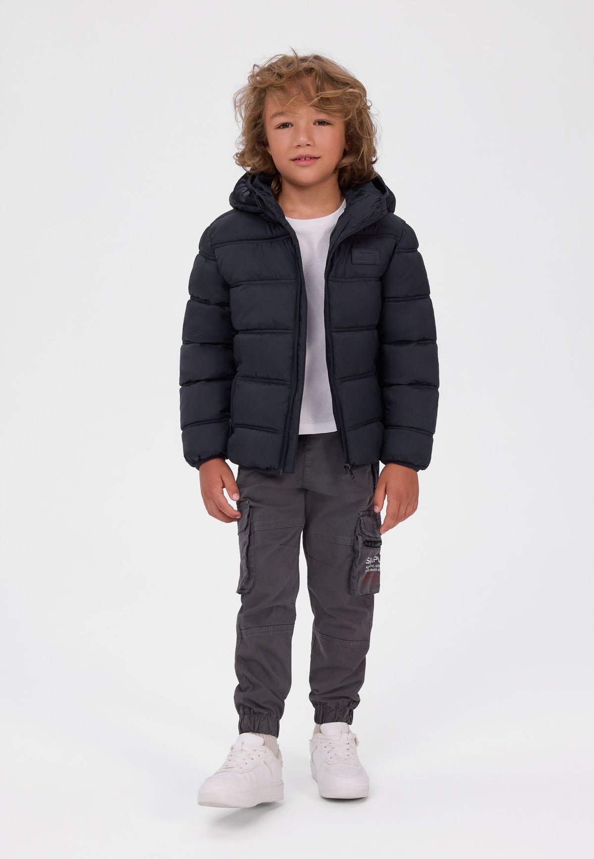 Boy wearing a short black hooded puffer jacket open over a white T-shirt.